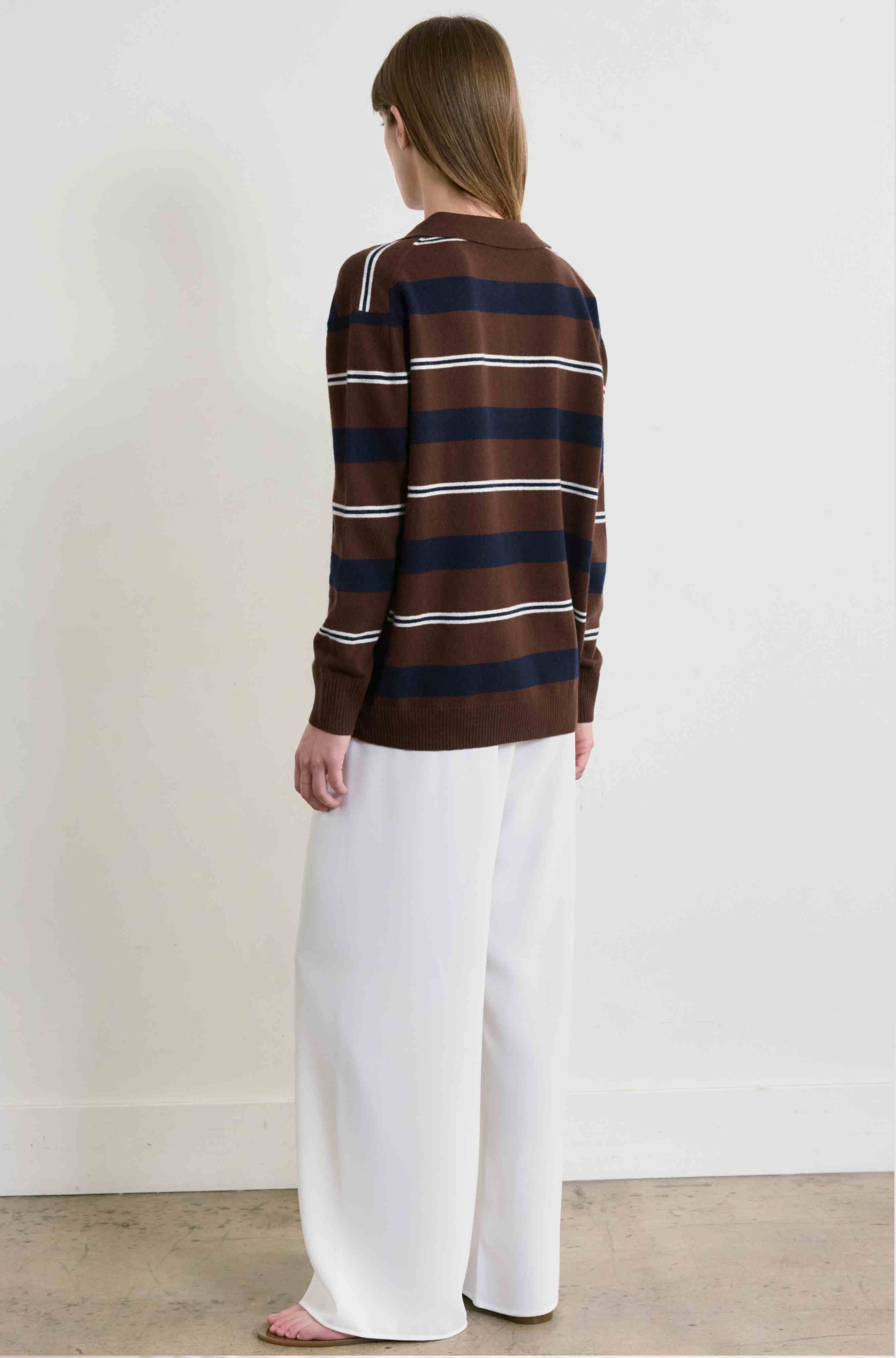 Person wearing a brown and blue striped sweater with white pants against a plain background