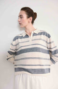 Woman wearing a striped sweater and white shirt against a plain background