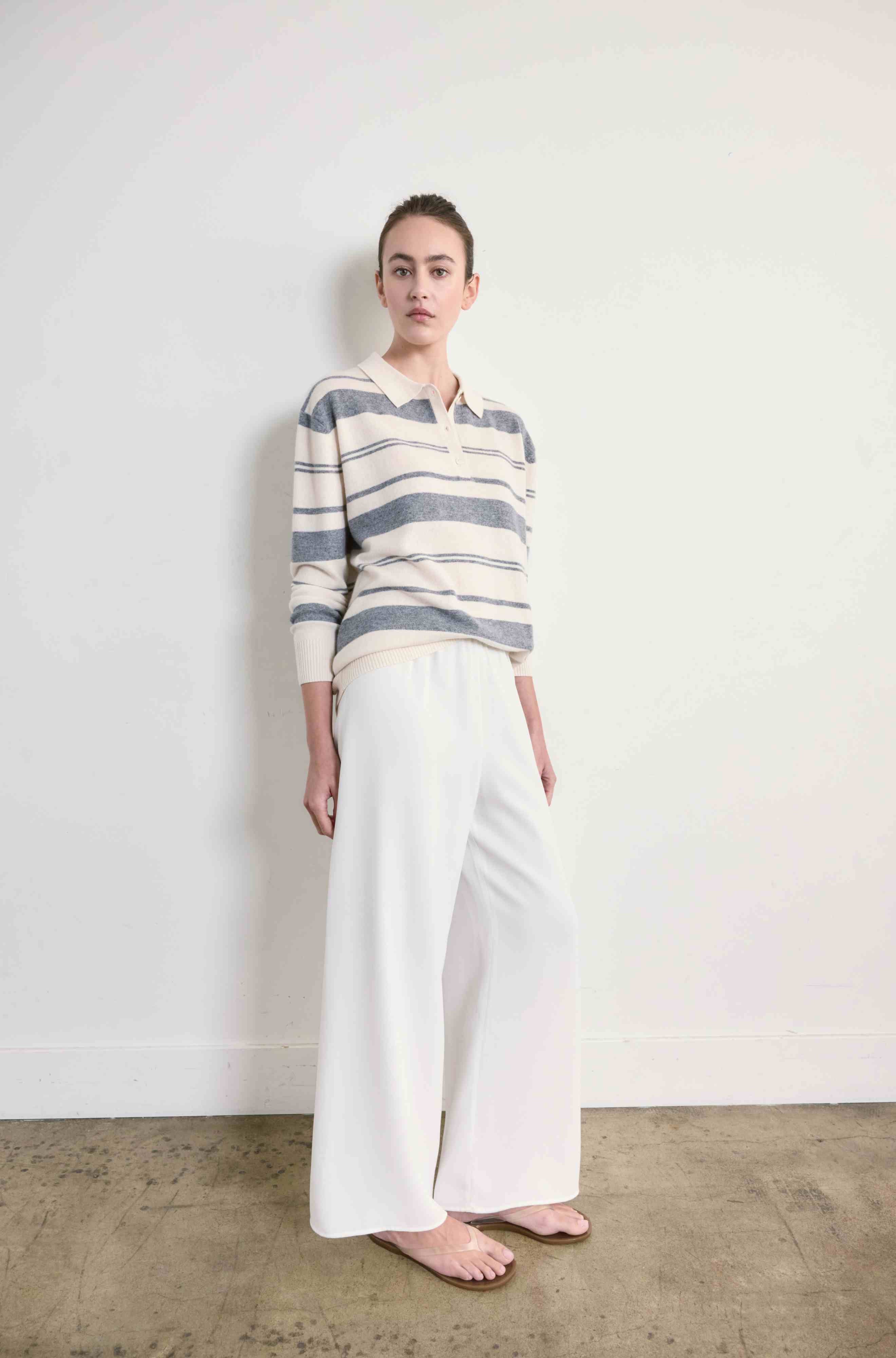 Person wearing a striped sweater and white pants against a plain background