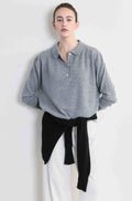 Person wearing a gray sweater with a black sweater tied around her waist and white pants on a plain background
