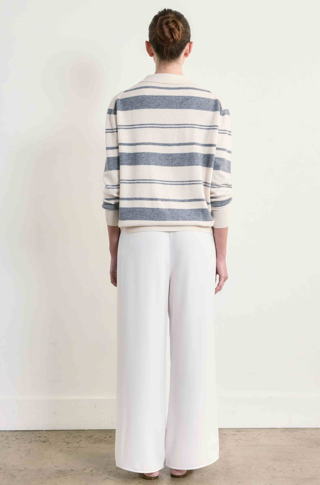 Person wearing a striped sweater and white pants against a plain background