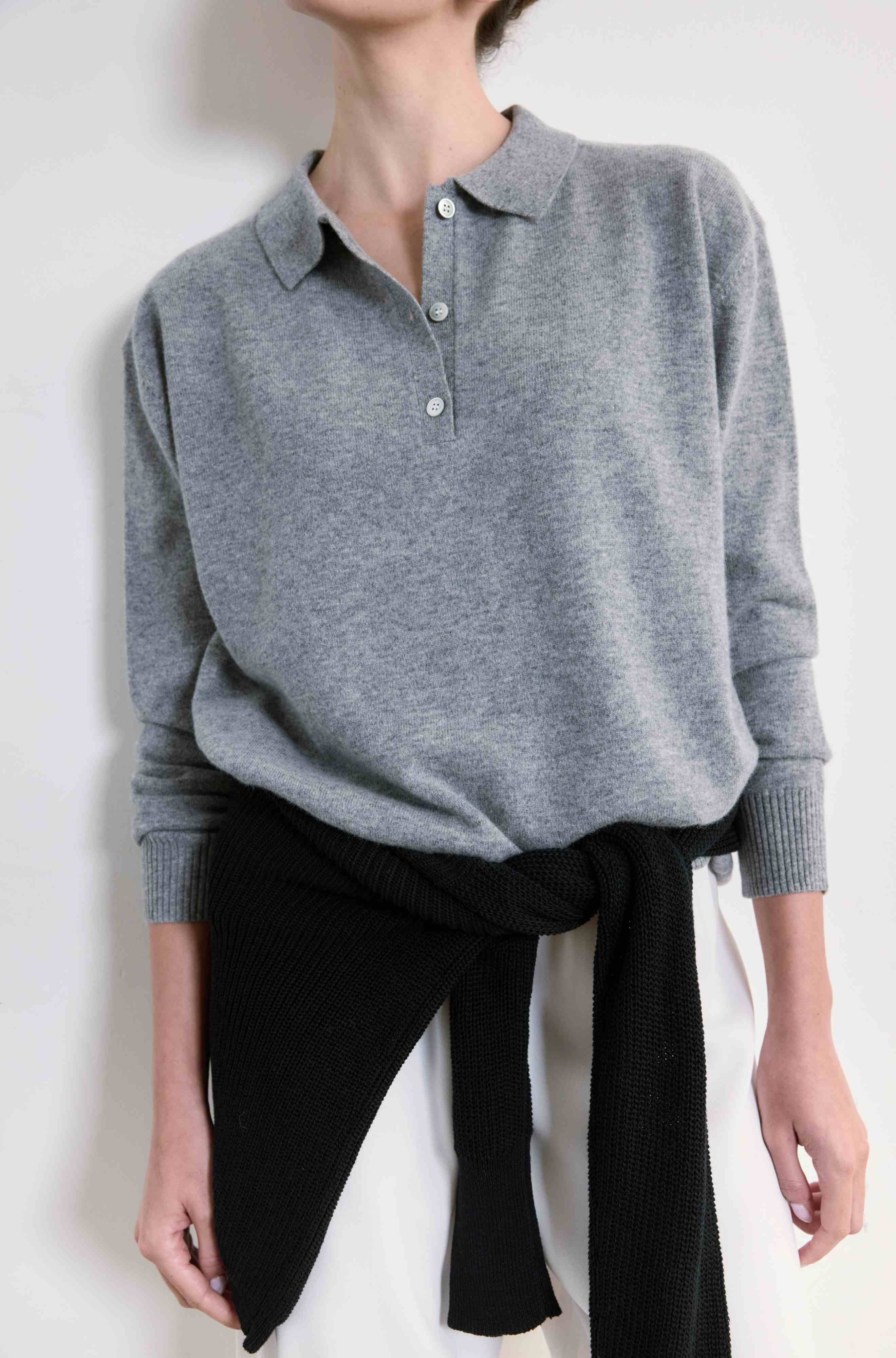 Person wearing a gray sweater and white pants against a white background