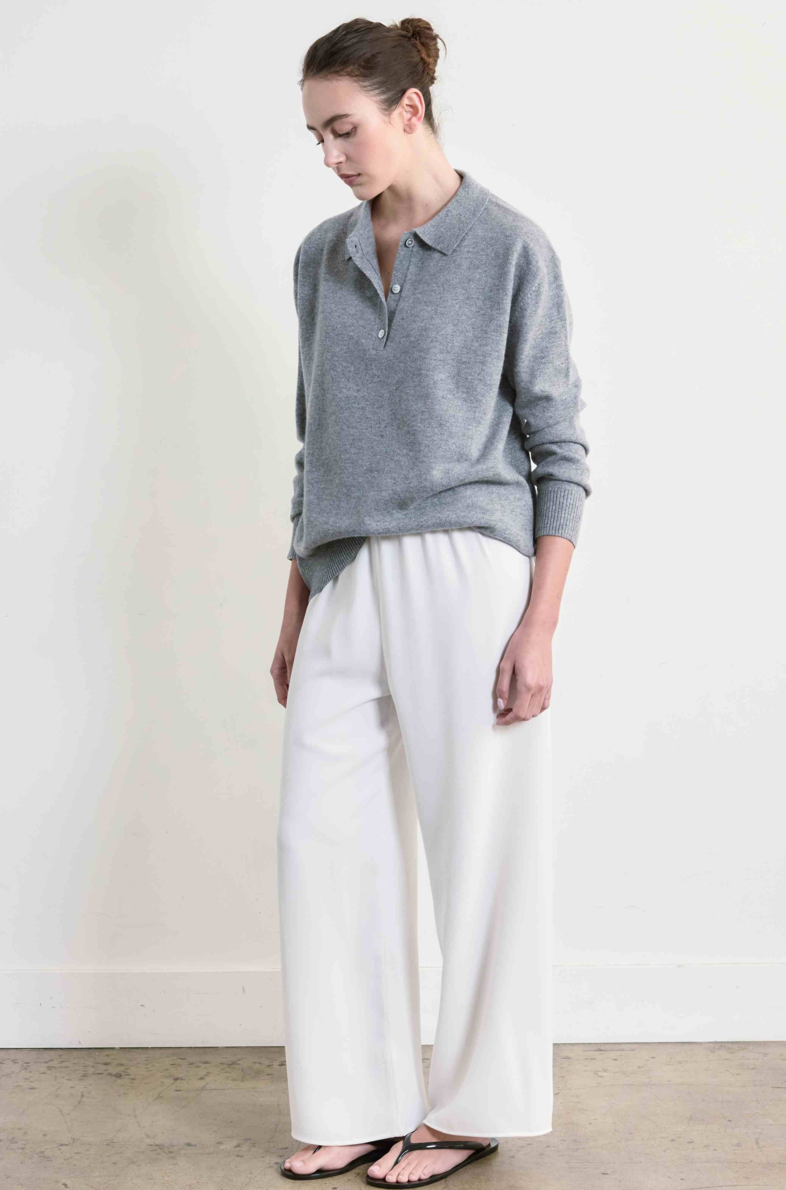 Woman wearing a gray sweater and white pants against a plain background