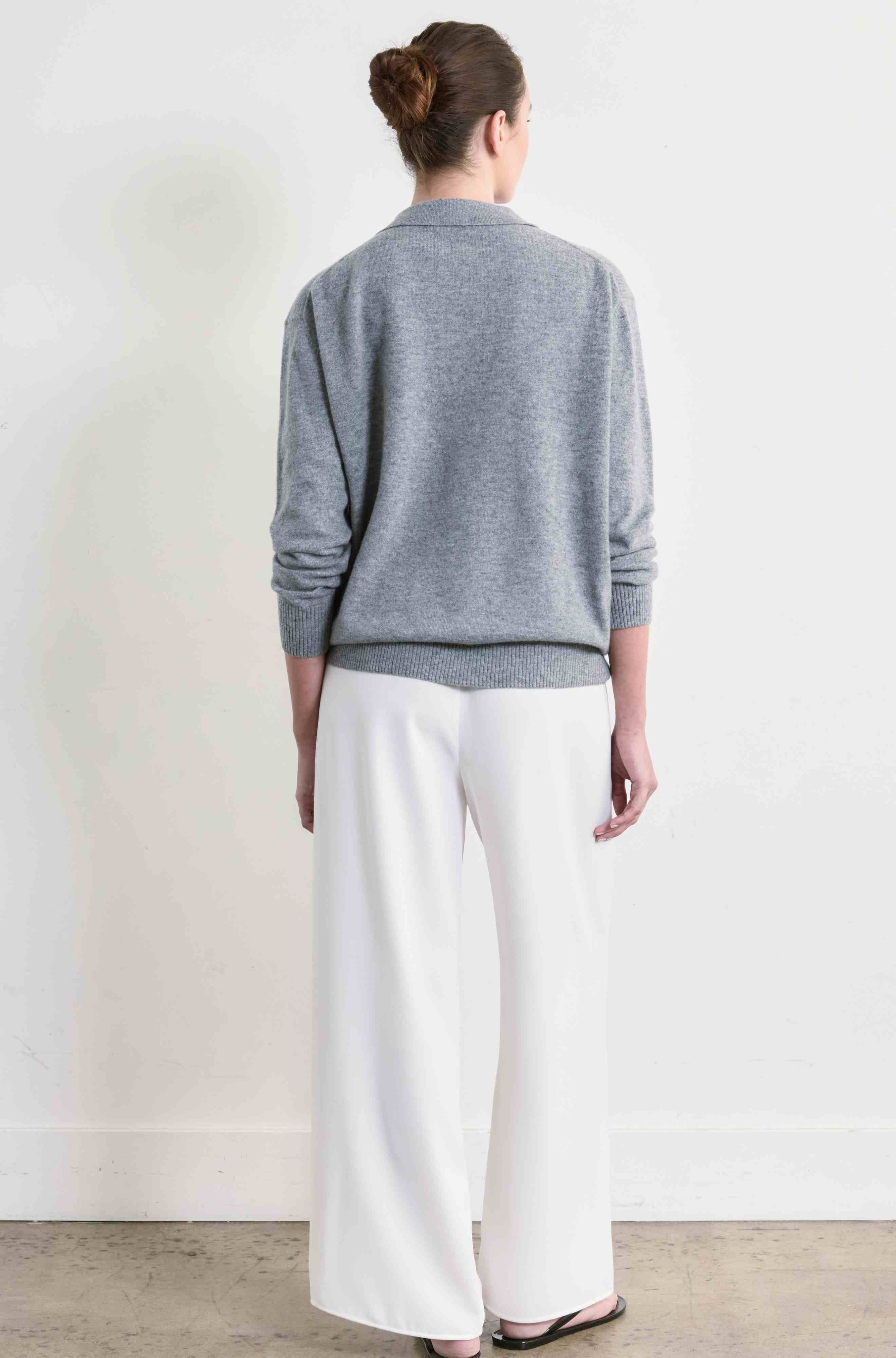 Person wearing a gray sweater and white pants against a plain background