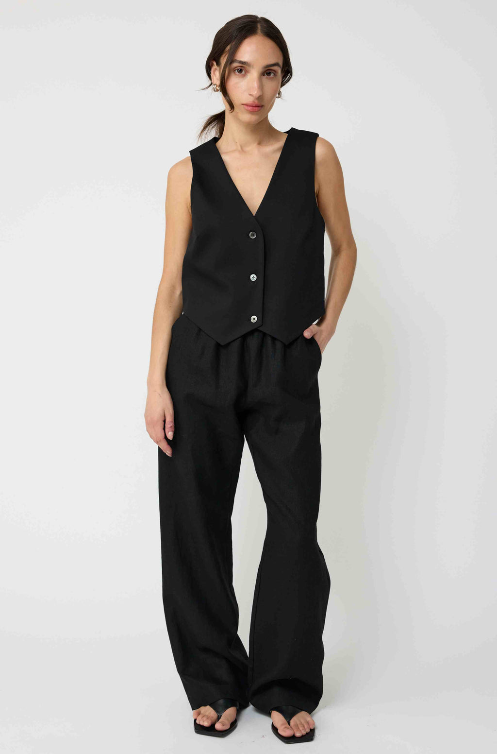 Woman wearing a black sleeveless top and wide-leg pants on a white background