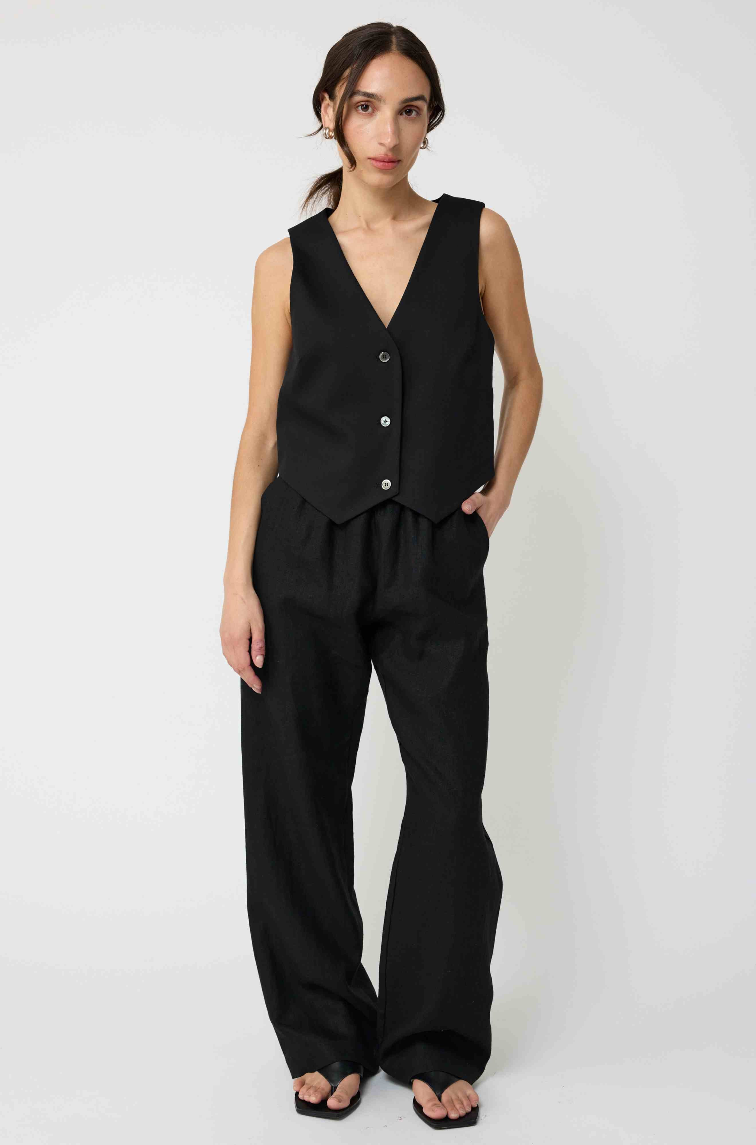 Woman wearing a black sleeveless top and wide-leg pants on a white background