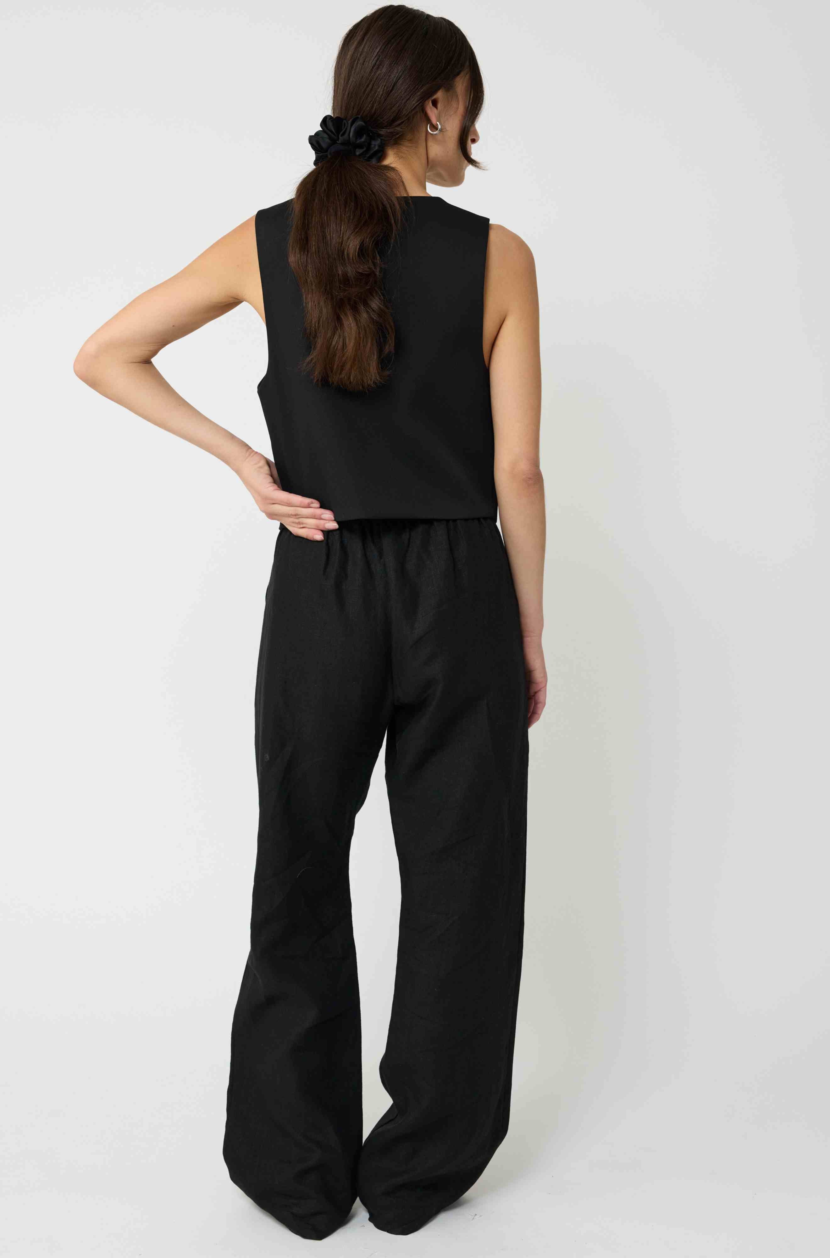 Woman wearing a black sleeveless top and wide-leg pants on a white background