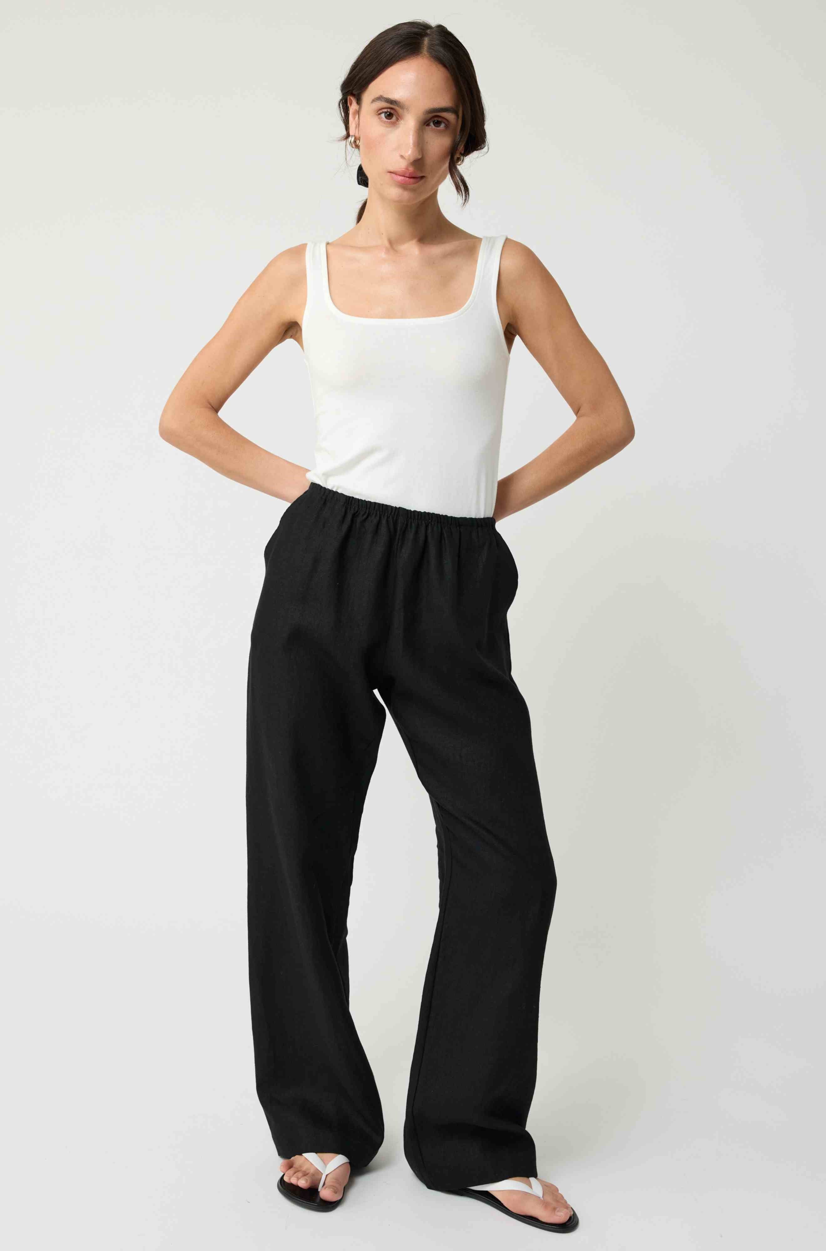 Woman wearing a white tank top and black wide-leg pants on a plain background