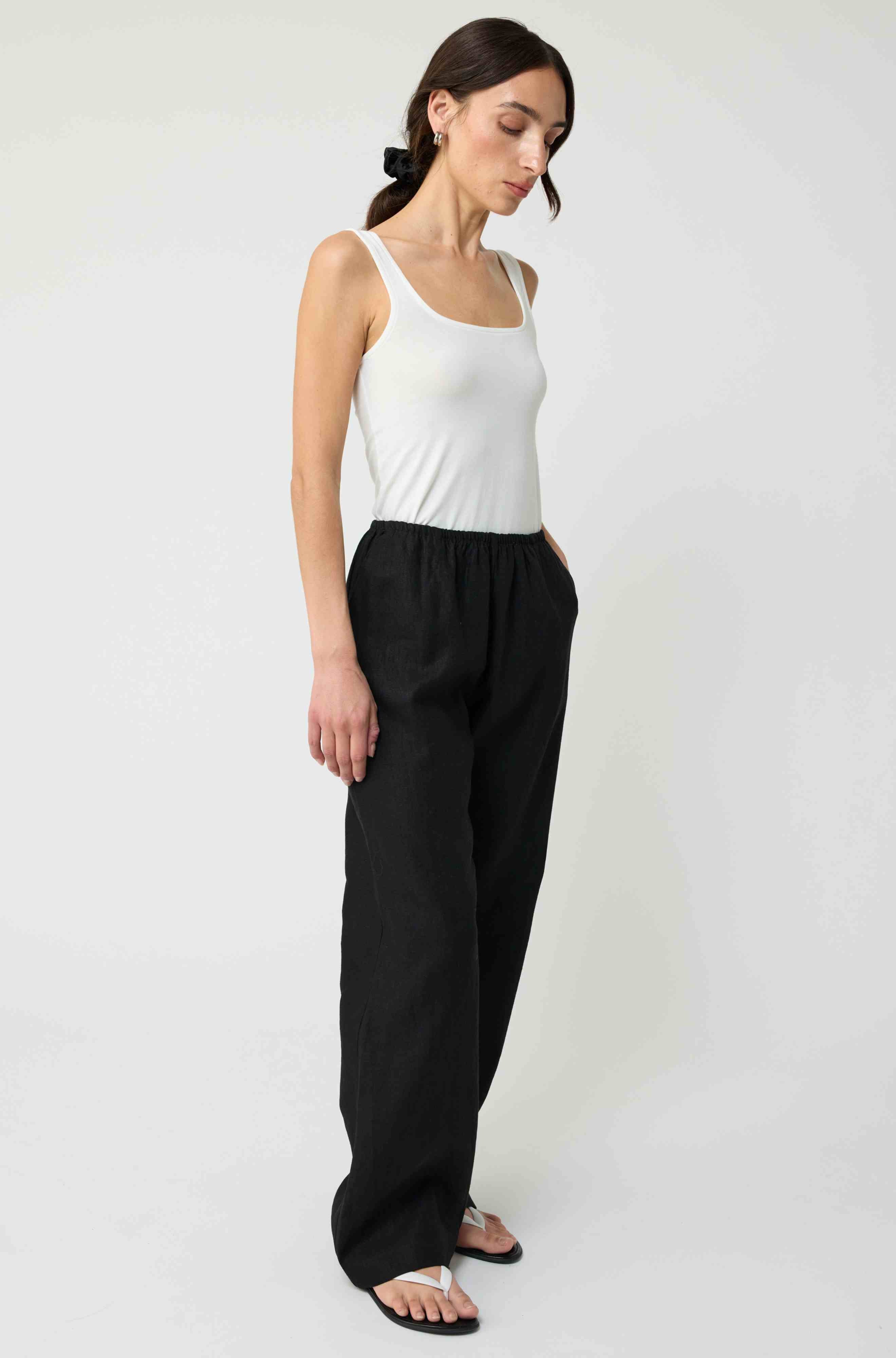 Woman wearing a white tank top and black pants on a white background