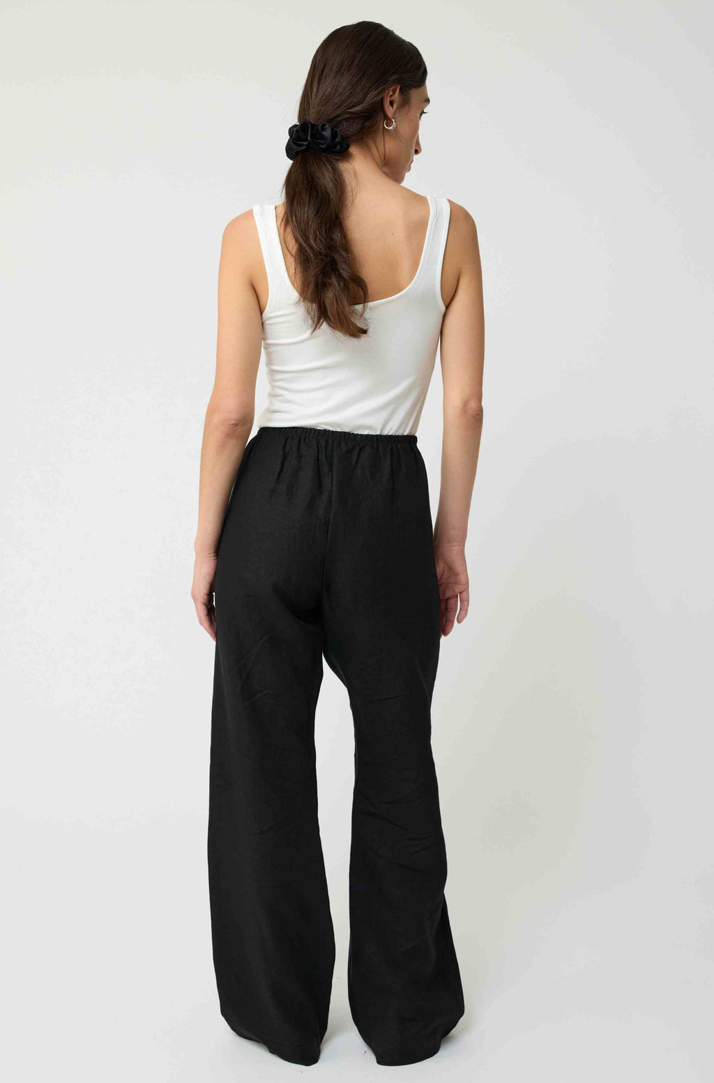 Woman wearing a white tank top and black wide-leg pants on a white background