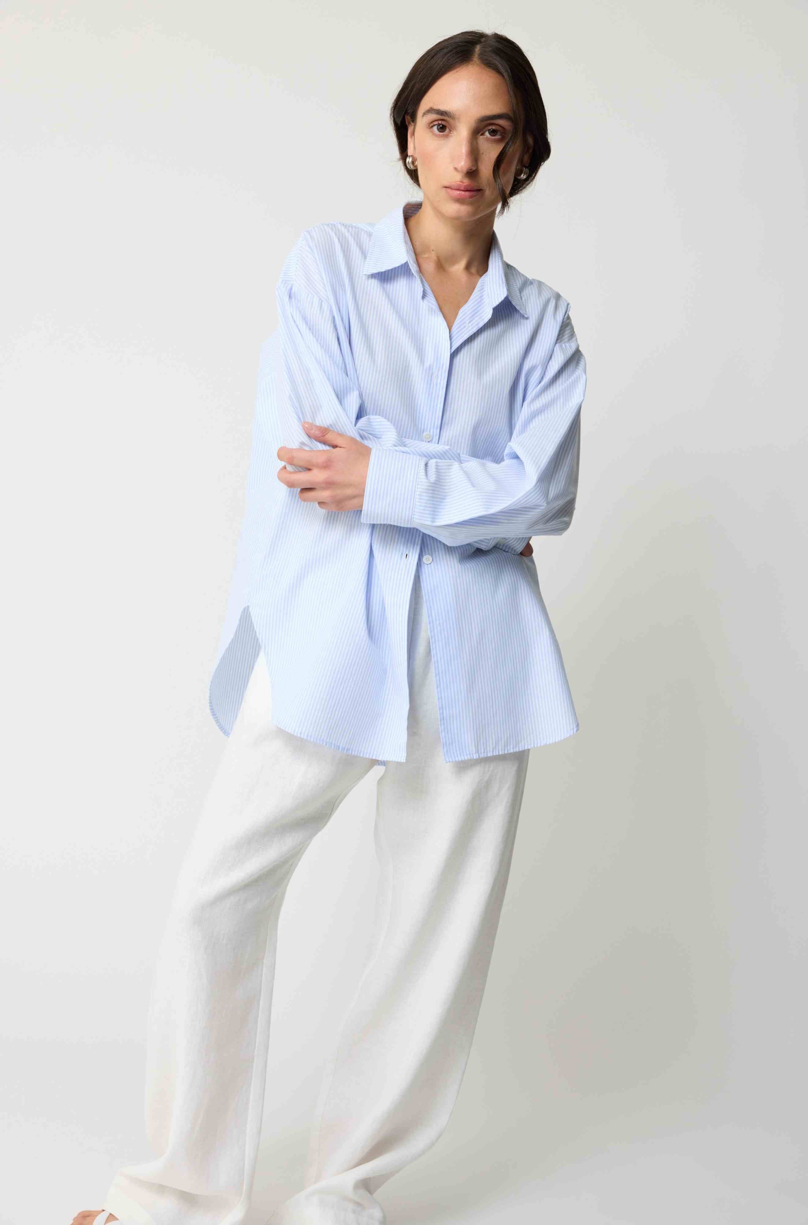 Person wearing a light blue shirt and white pants on a plain background