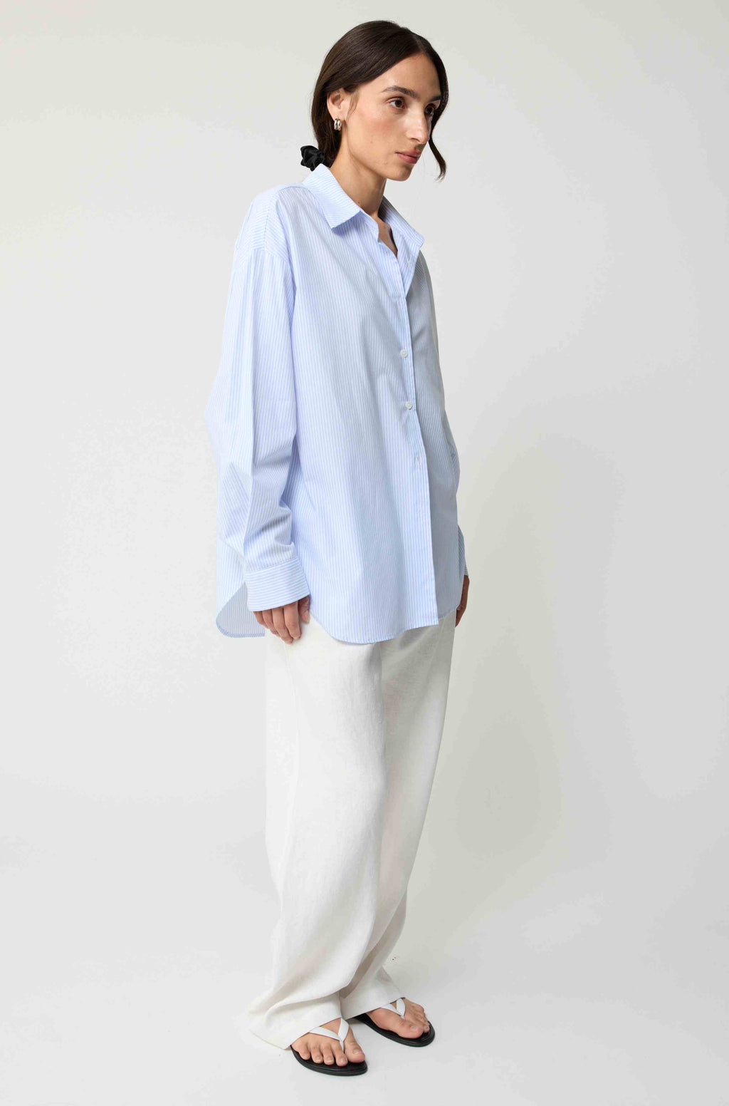 Woman wearing a light blue shirt and white pants on a plain background