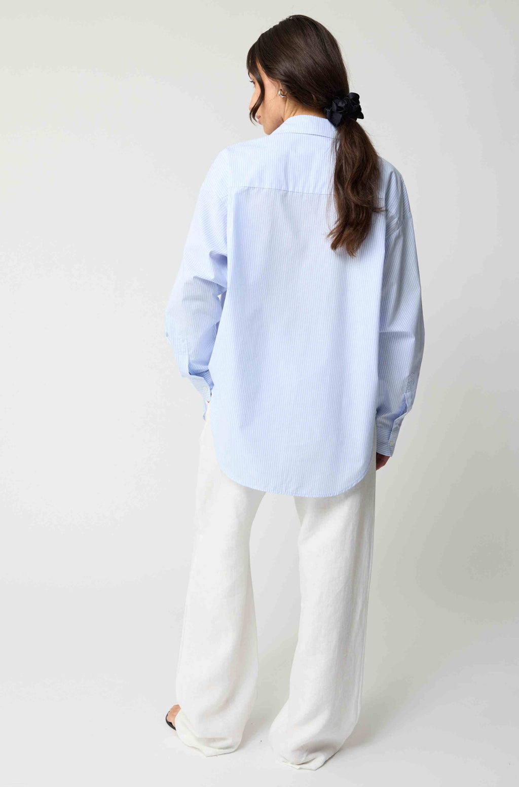 Person wearing a light blue oversized shirt and white pants on a plain background