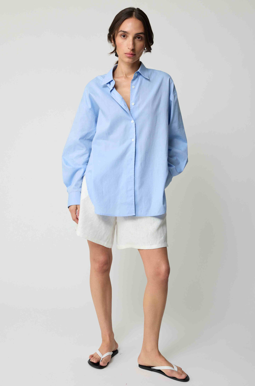 Woman wearing a light blue shirt and white shorts on a plain background