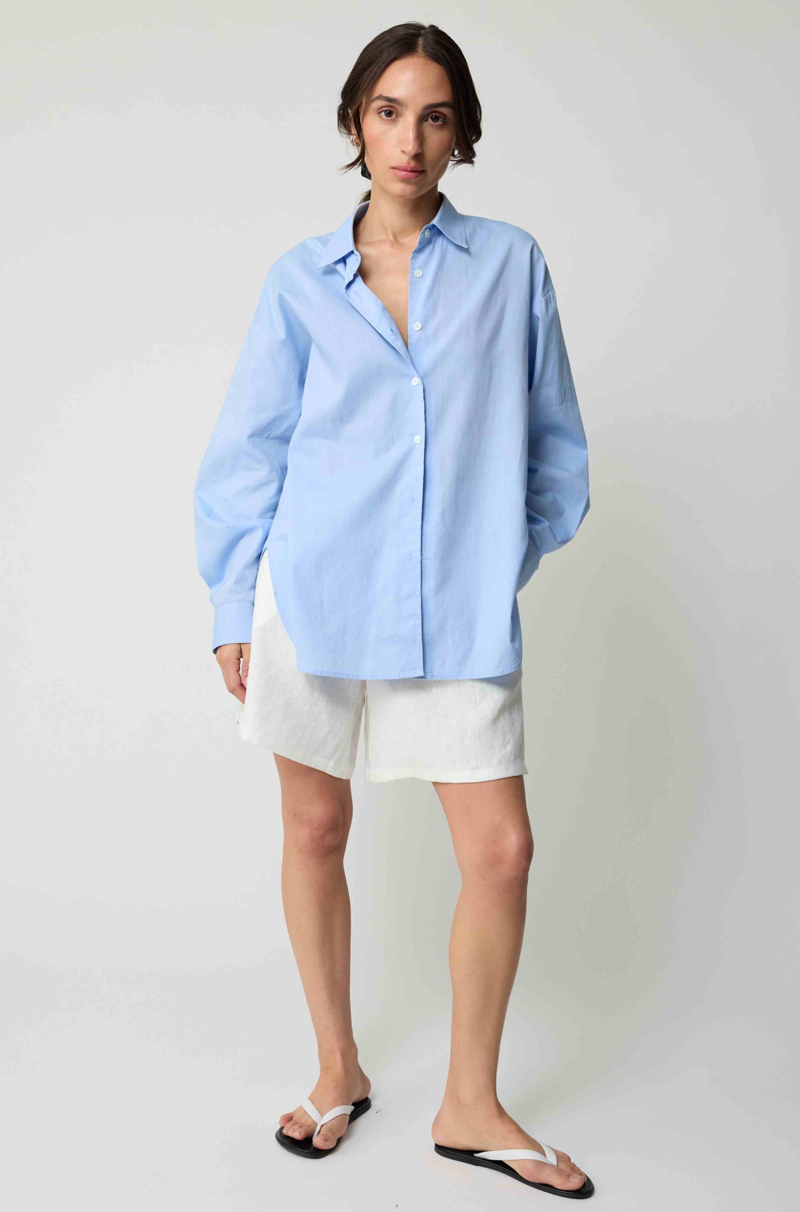 Woman wearing a light blue shirt and white shorts on a plain background