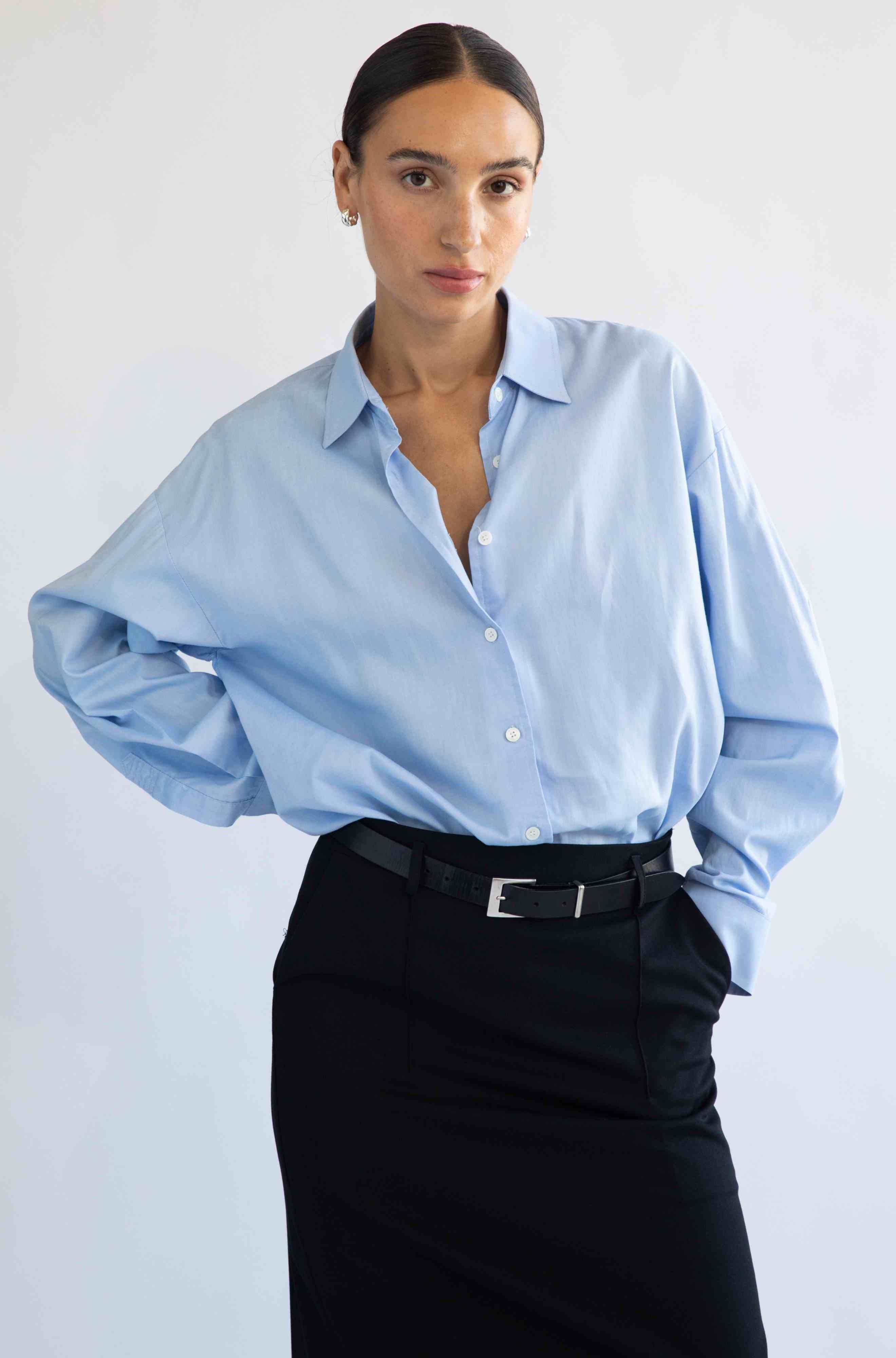 Woman wearing a light blue shirt and black skirt against a white background
