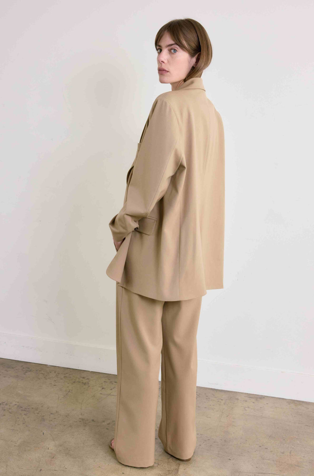 Woman wearing a beige suit standing against a white wall.