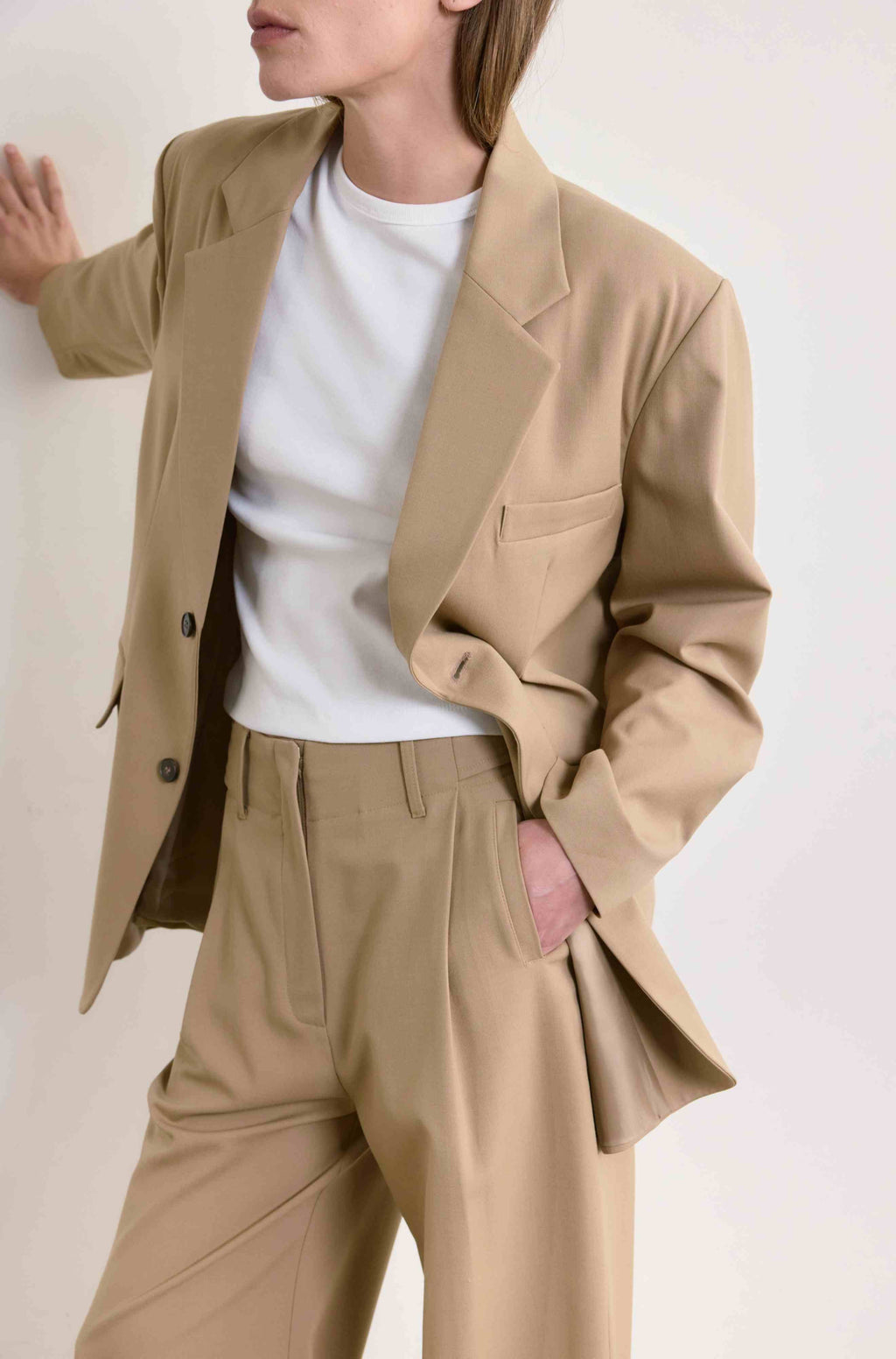 Person wearing a beige blazer and pants with a white shirt on a light background