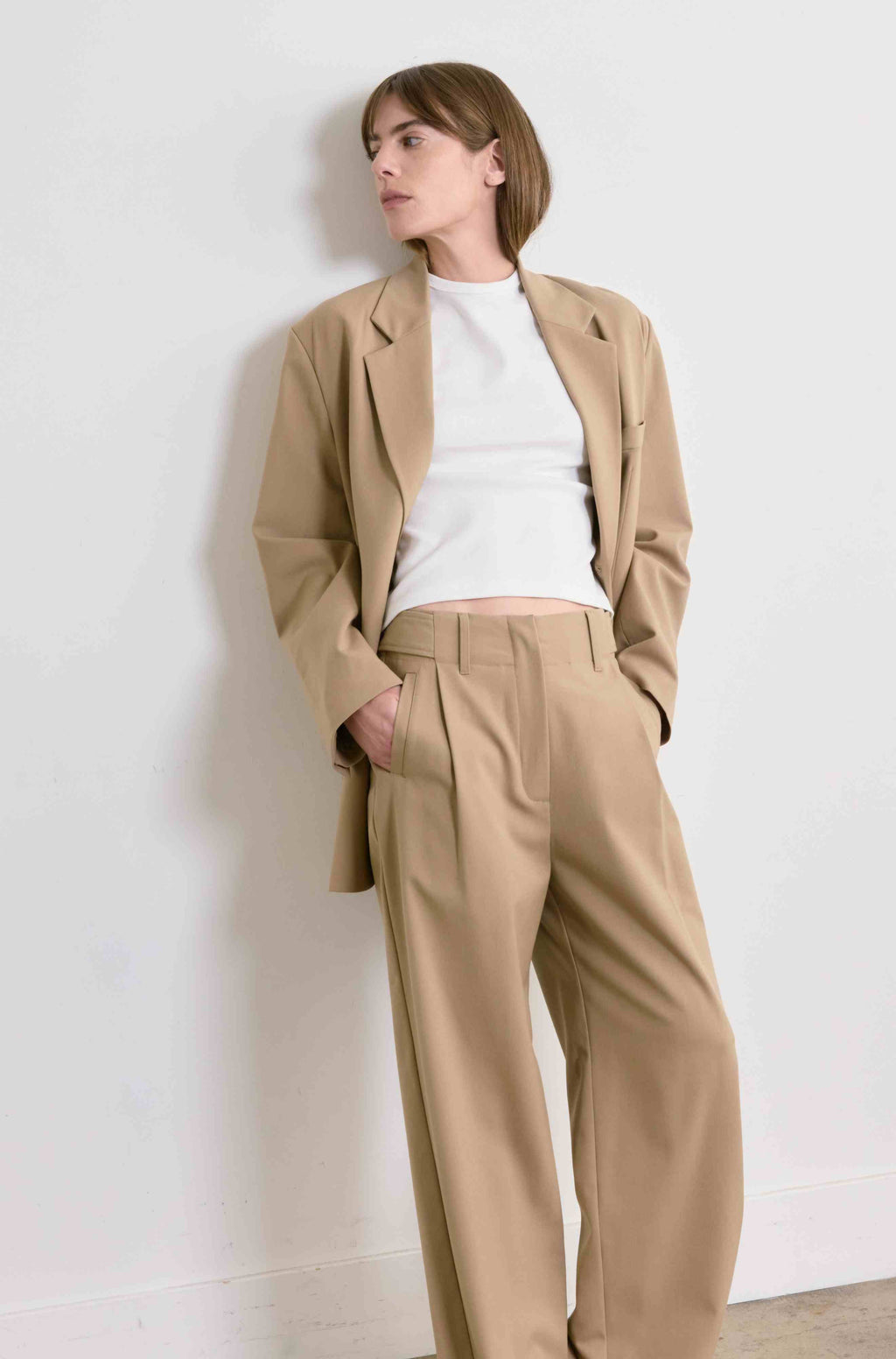 Woman wearing a beige suit and white shirt against a white wall