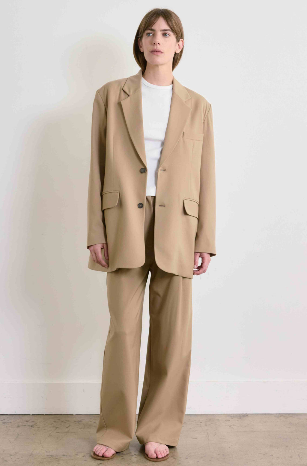 Person wearing a beige suit standing against a plain background