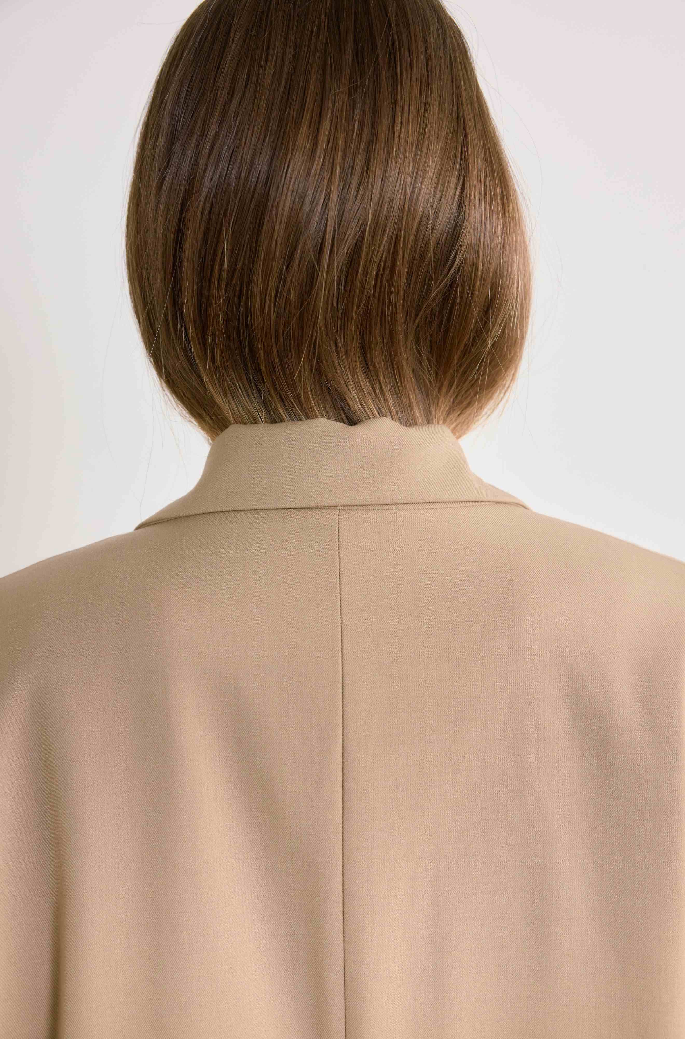 Person wearing a beige coat with a plain background