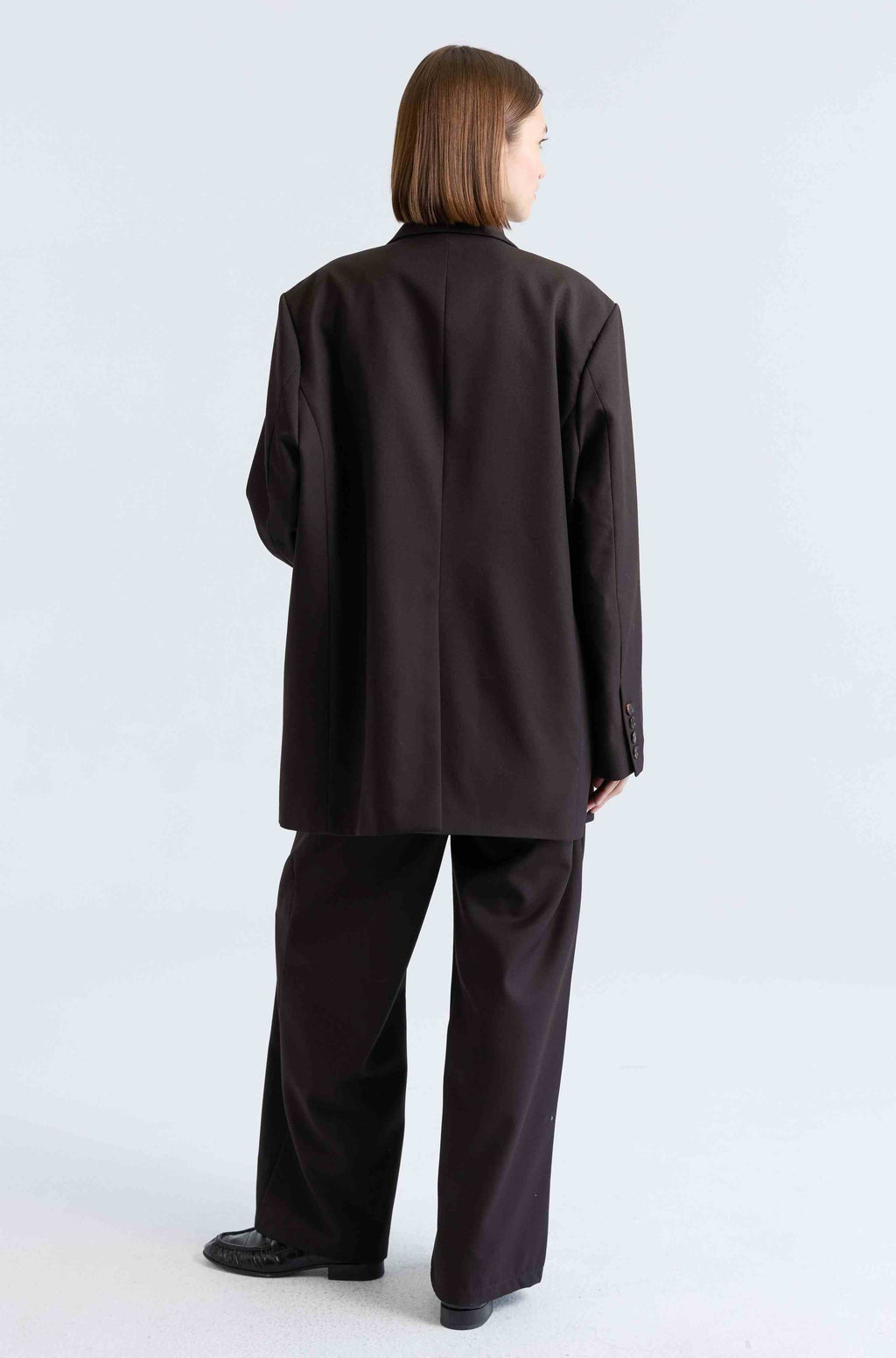 Woman wearing a dark brown suit set on a light grey background