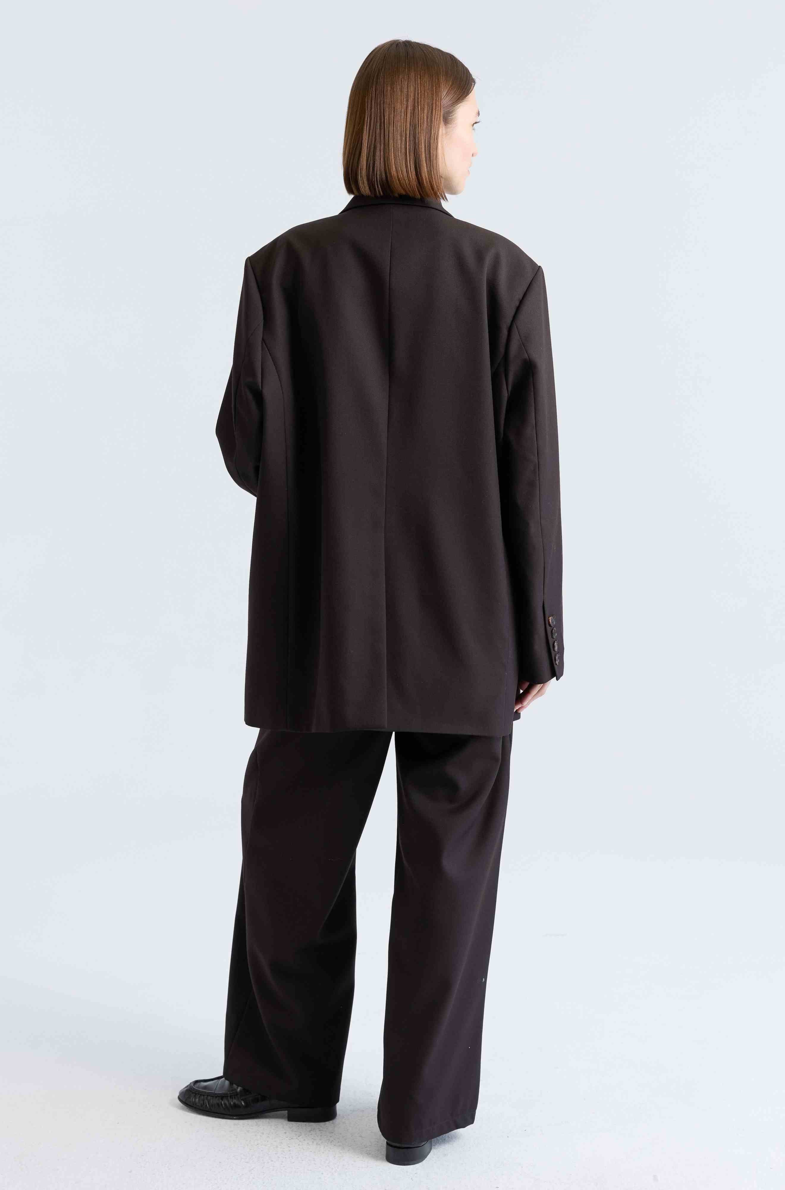 Woman wearing a dark brown suit set on a light grey background