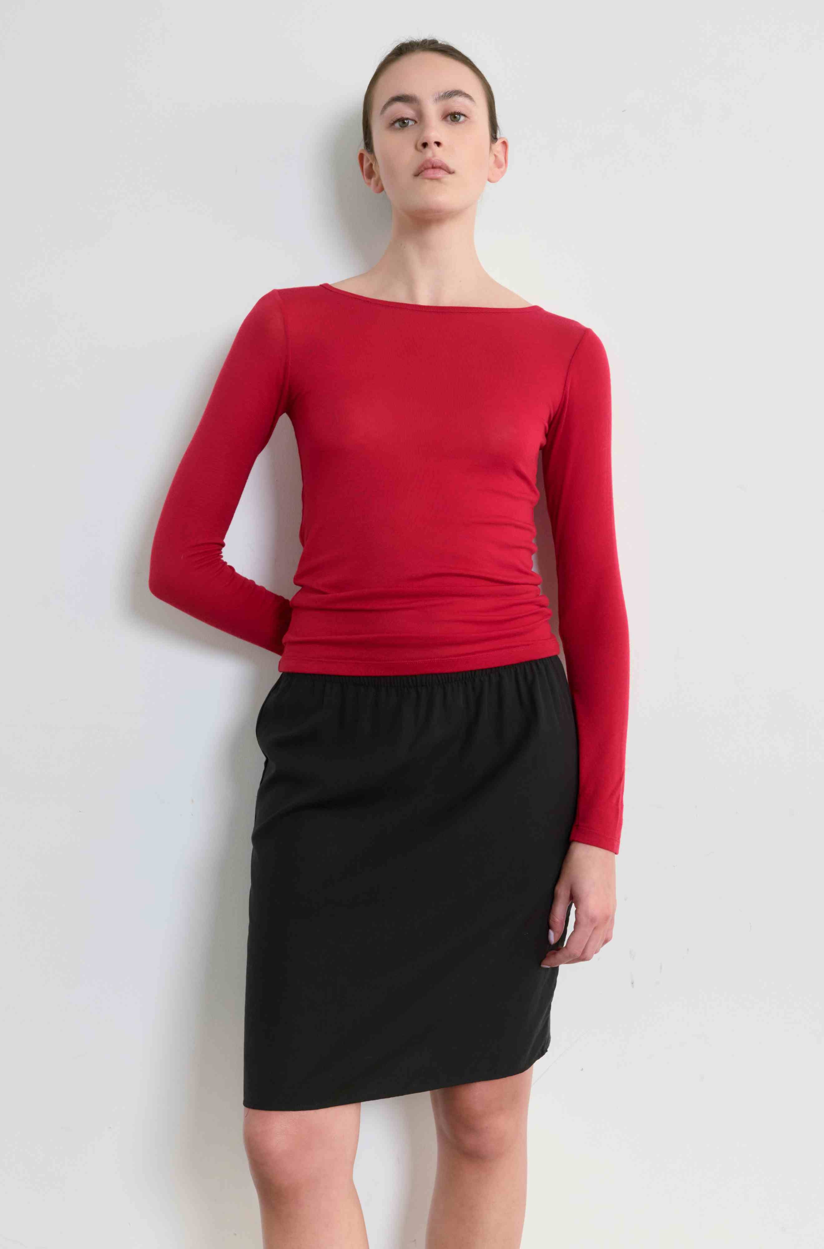 Person wearing a red long-sleeve top and black skirt on a white background