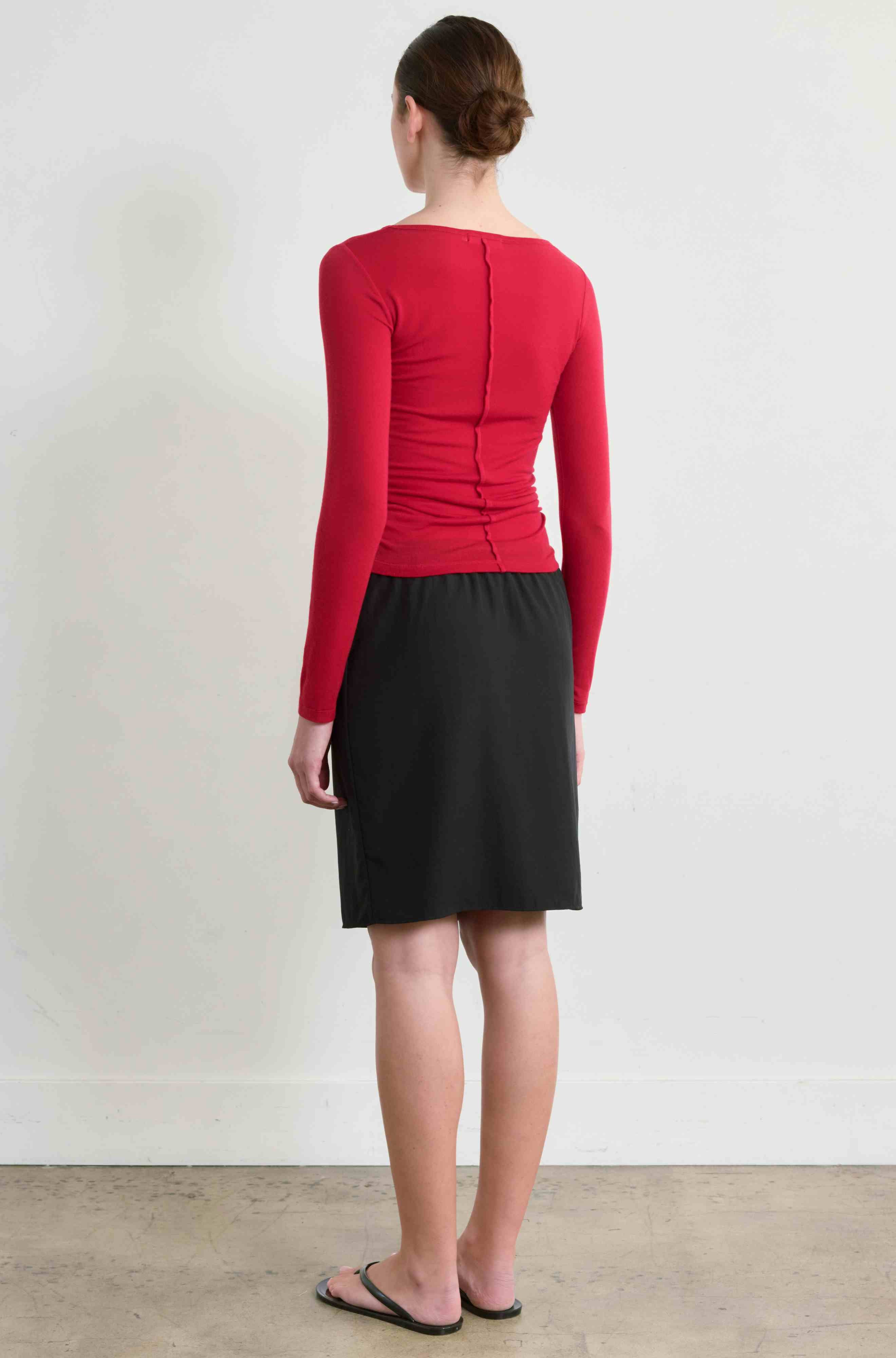 Person wearing a red top and black skirt against a white background