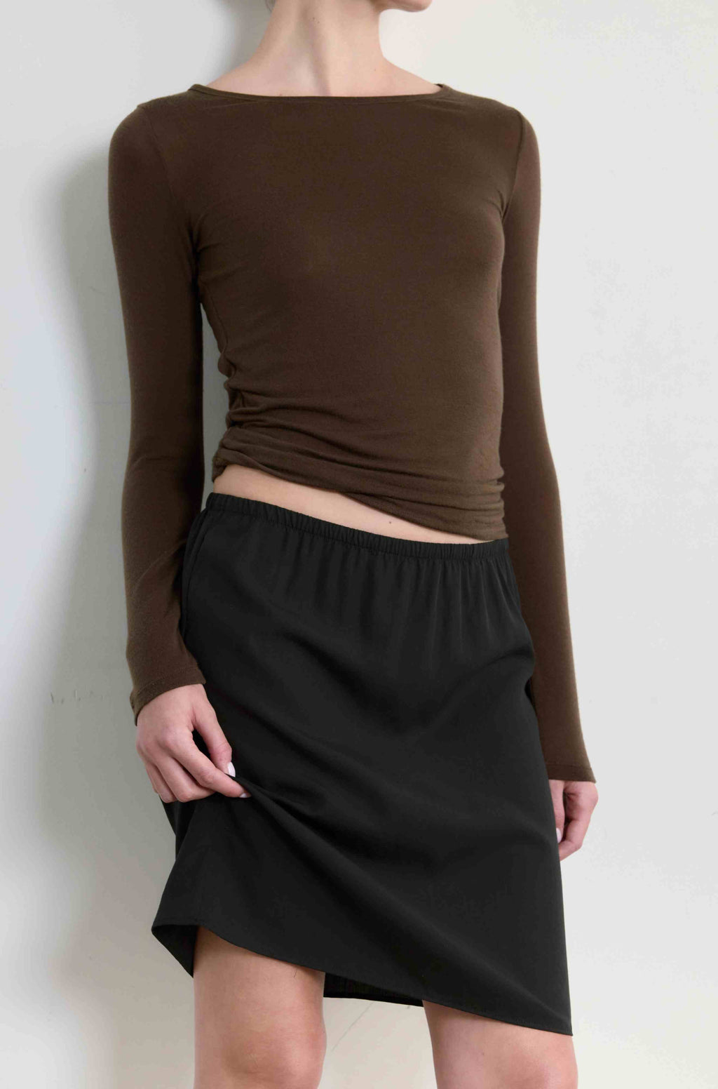 Person wearing a brown long-sleeve top and black skirt against a white background