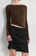 Person wearing a brown long-sleeve top and black skirt against a white background