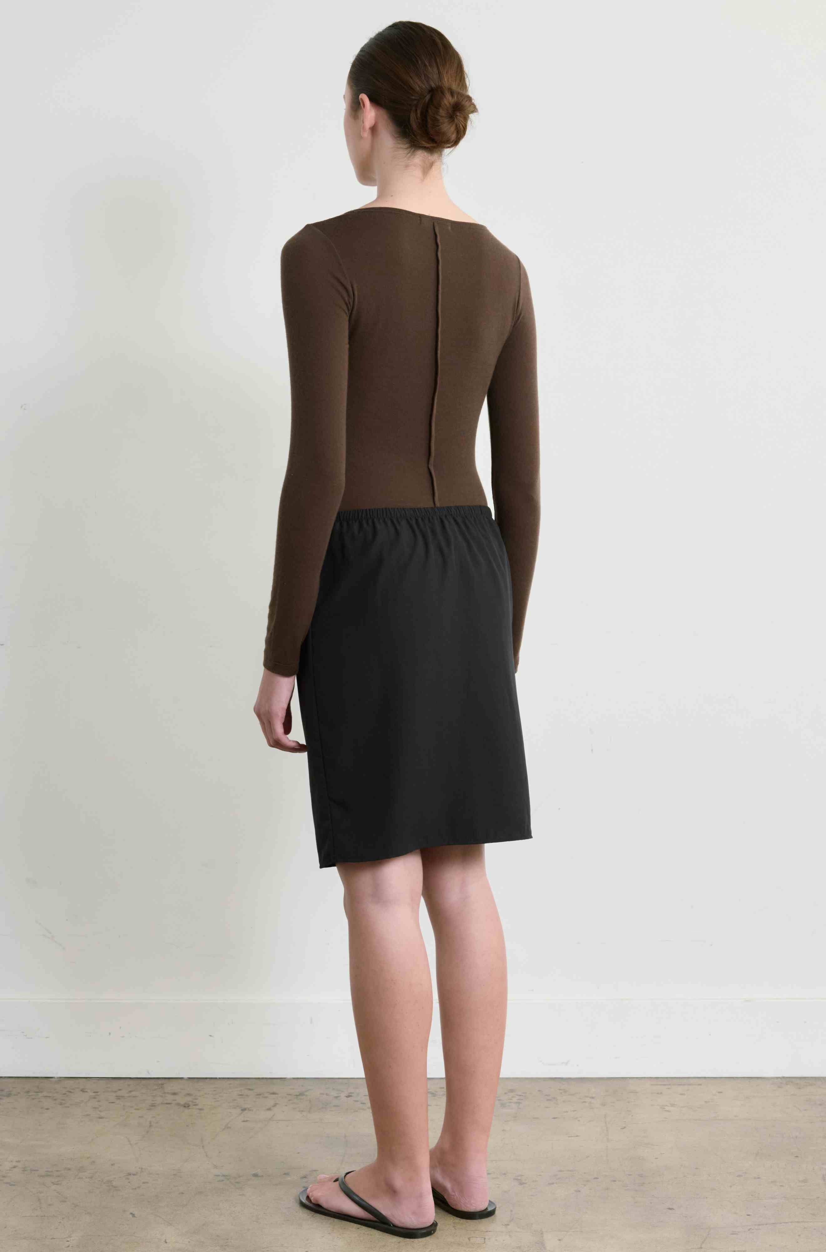 Person wearing a brown long-sleeve top and black skirt against a white background