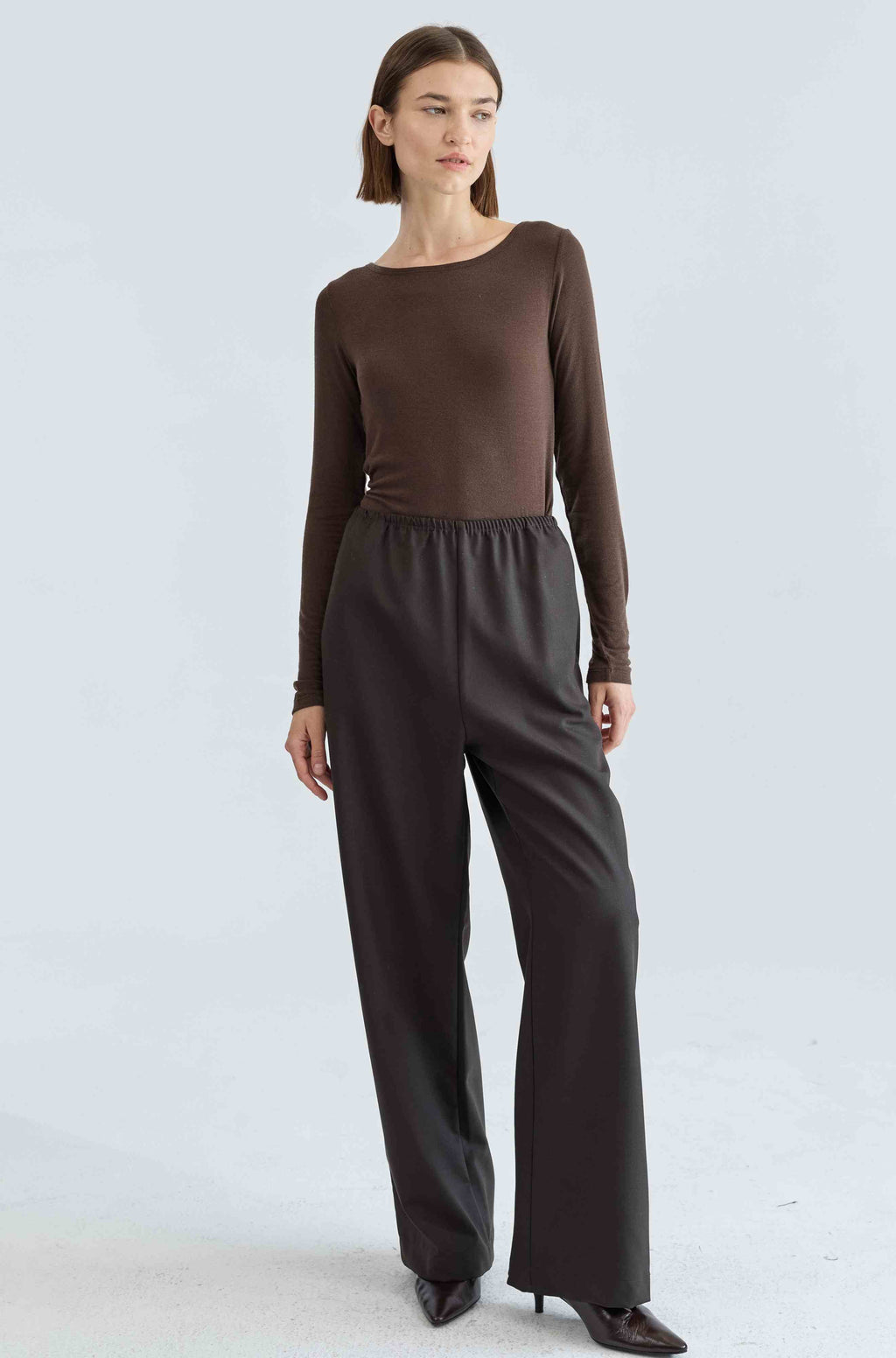 Woman wearing a brown long-sleeve top and wide-leg pants on a light gray background