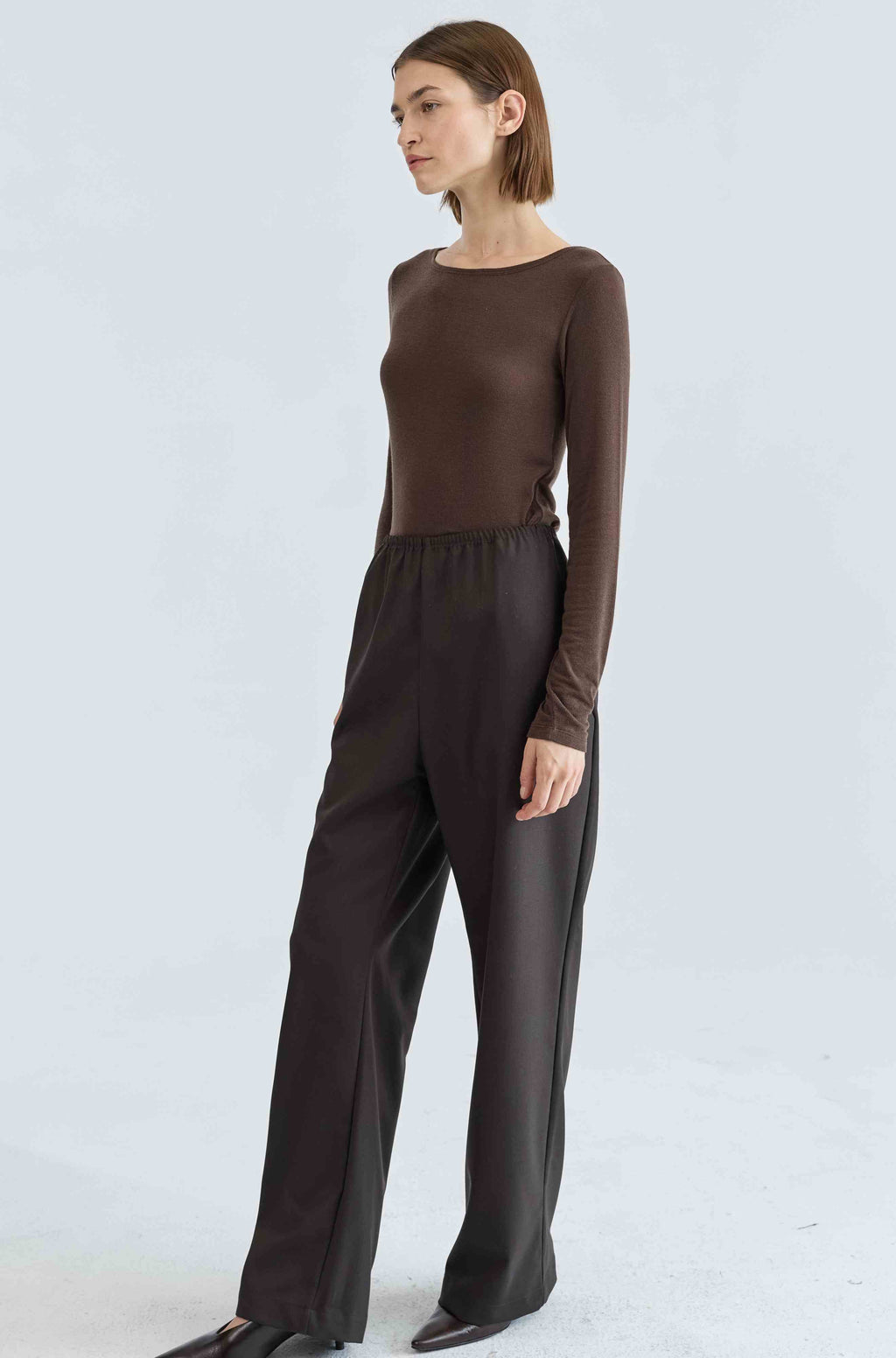 Woman wearing a brown long-sleeve top and wide-leg pants on a white background
