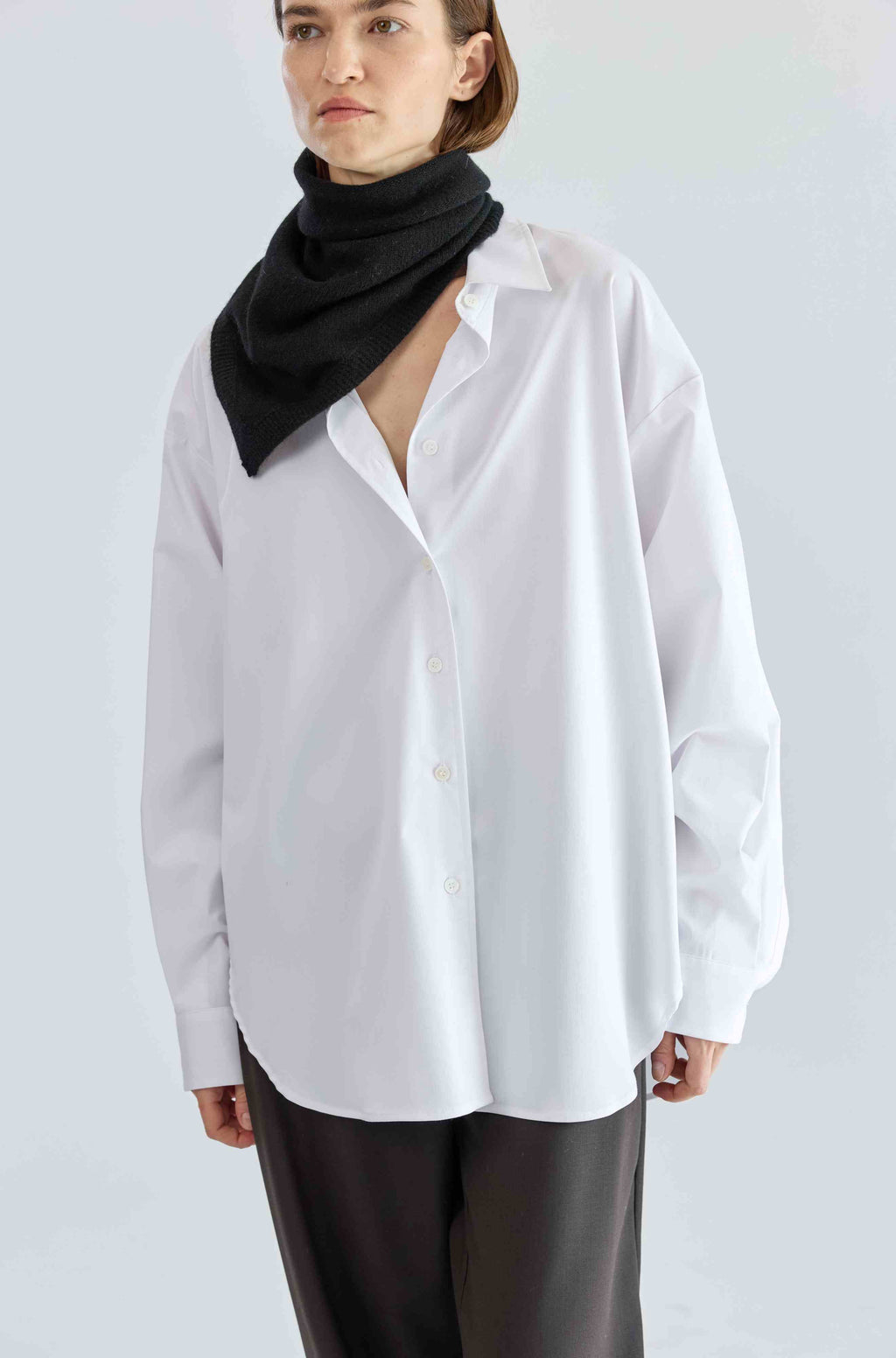 Person wearing a white shirt with a black scarf on a light gray background