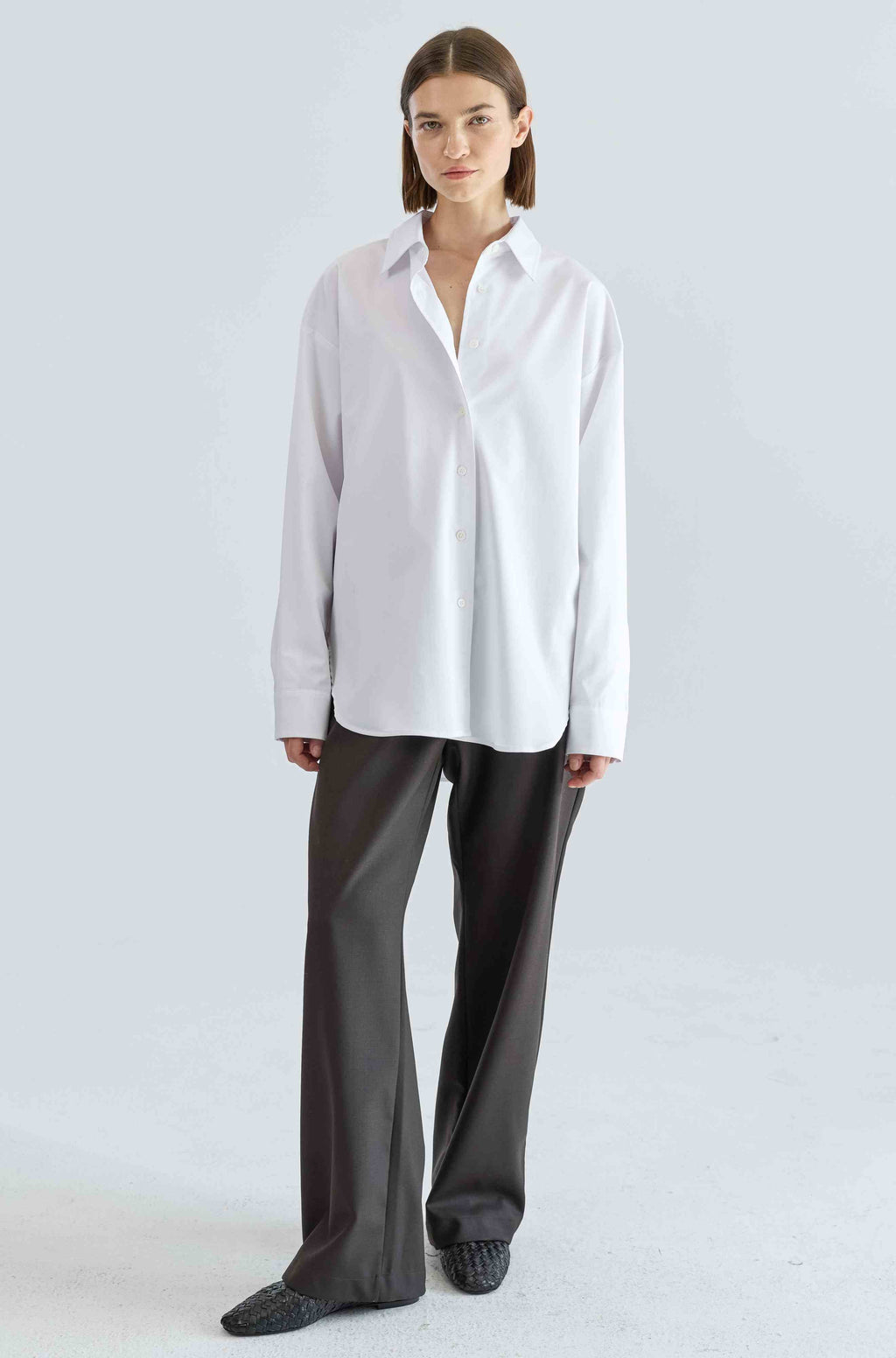 Person wearing a white shirt and dark pants on a light gray background
