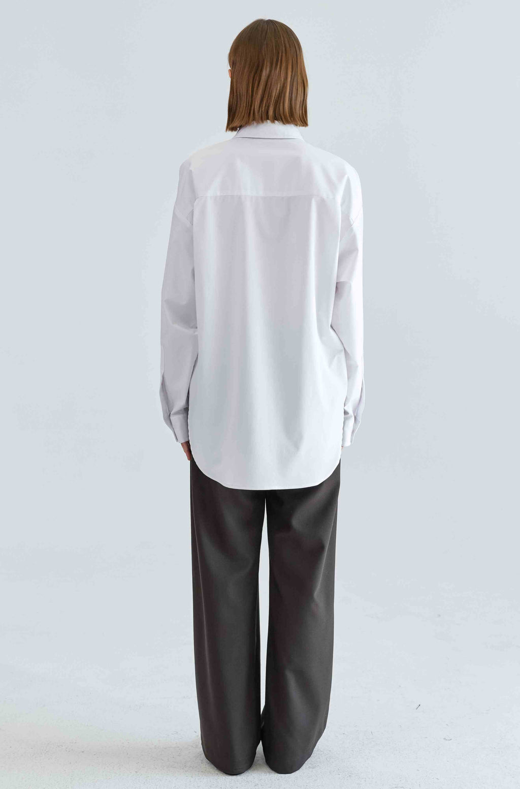 Person wearing a white shirt and dark pants on a light gray background