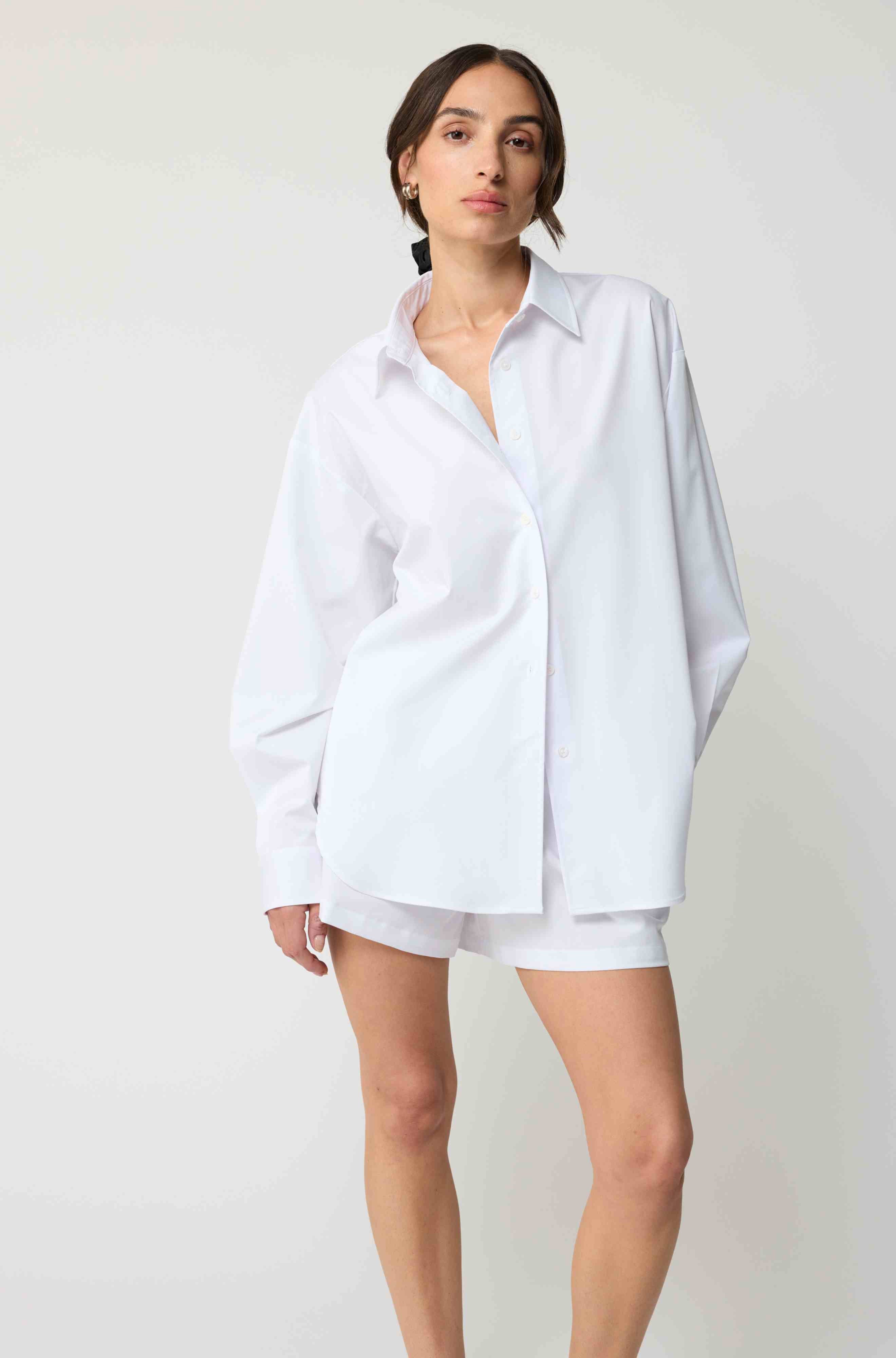 Woman wearing a white oversized shirt and shorts on a plain background