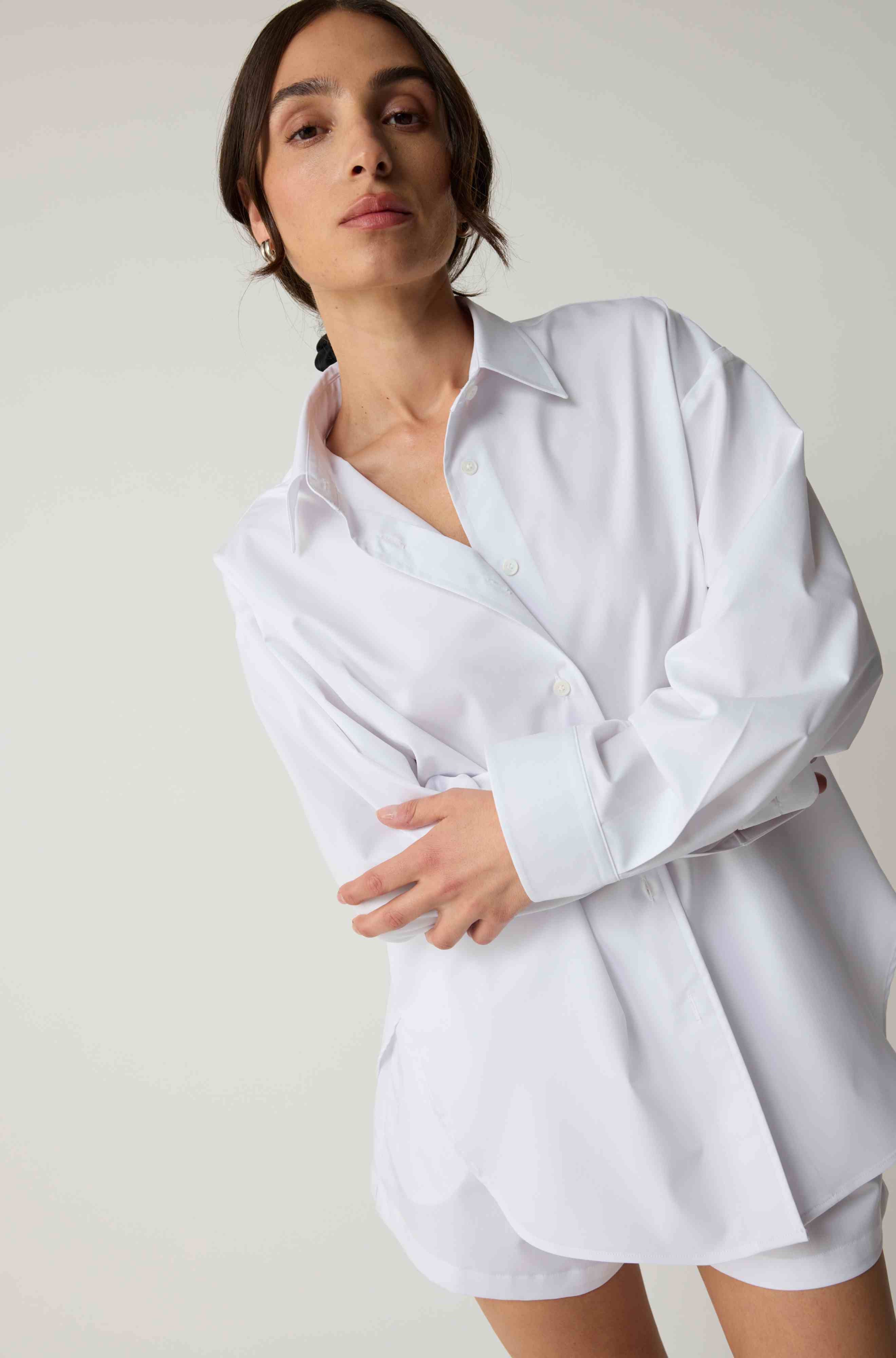 Woman wearing a white oversized shirt against a plain background