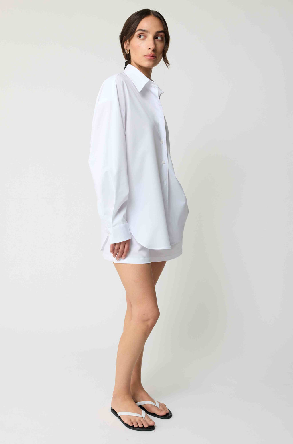 Woman wearing a white oversized shirt against a plain background