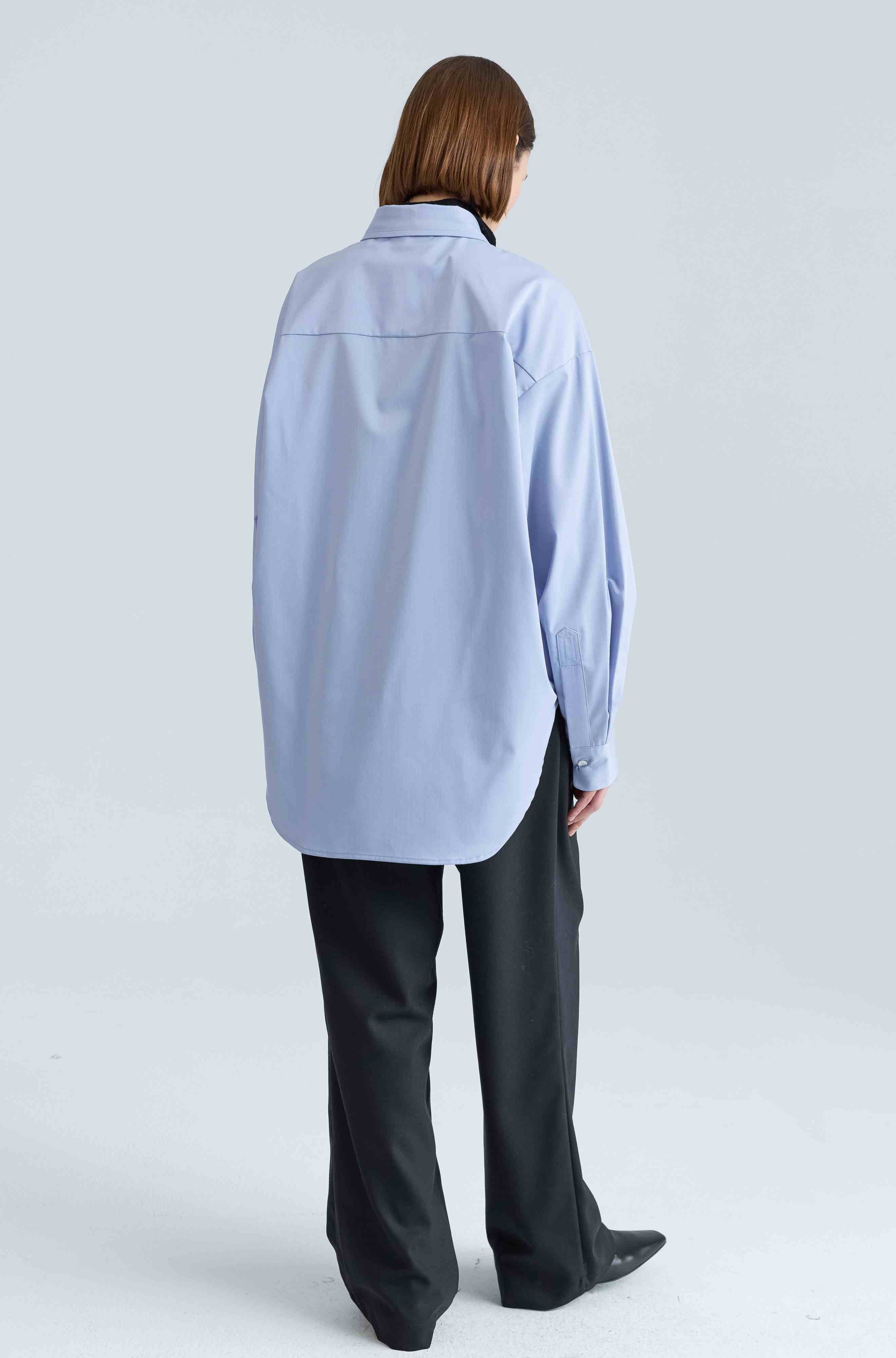 Person wearing a light blue shirt and black pants on a white background