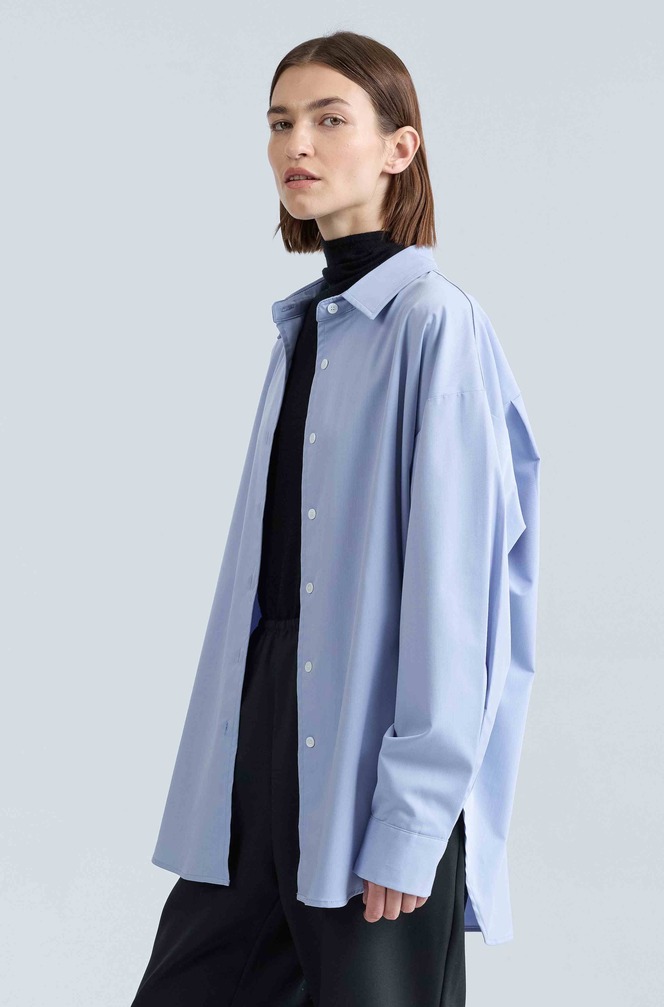 Woman wearing a light blue shirt over a black turtleneck on a light gray background