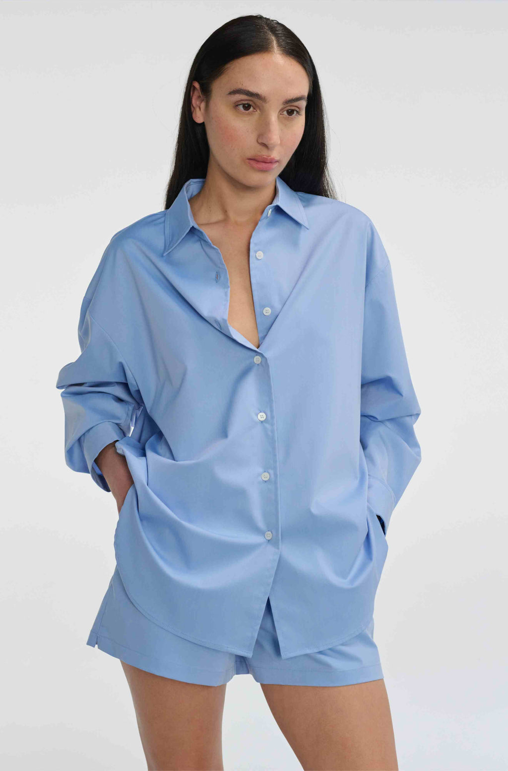 Woman wearing a light blue oversized shirt and shorts on a white background
