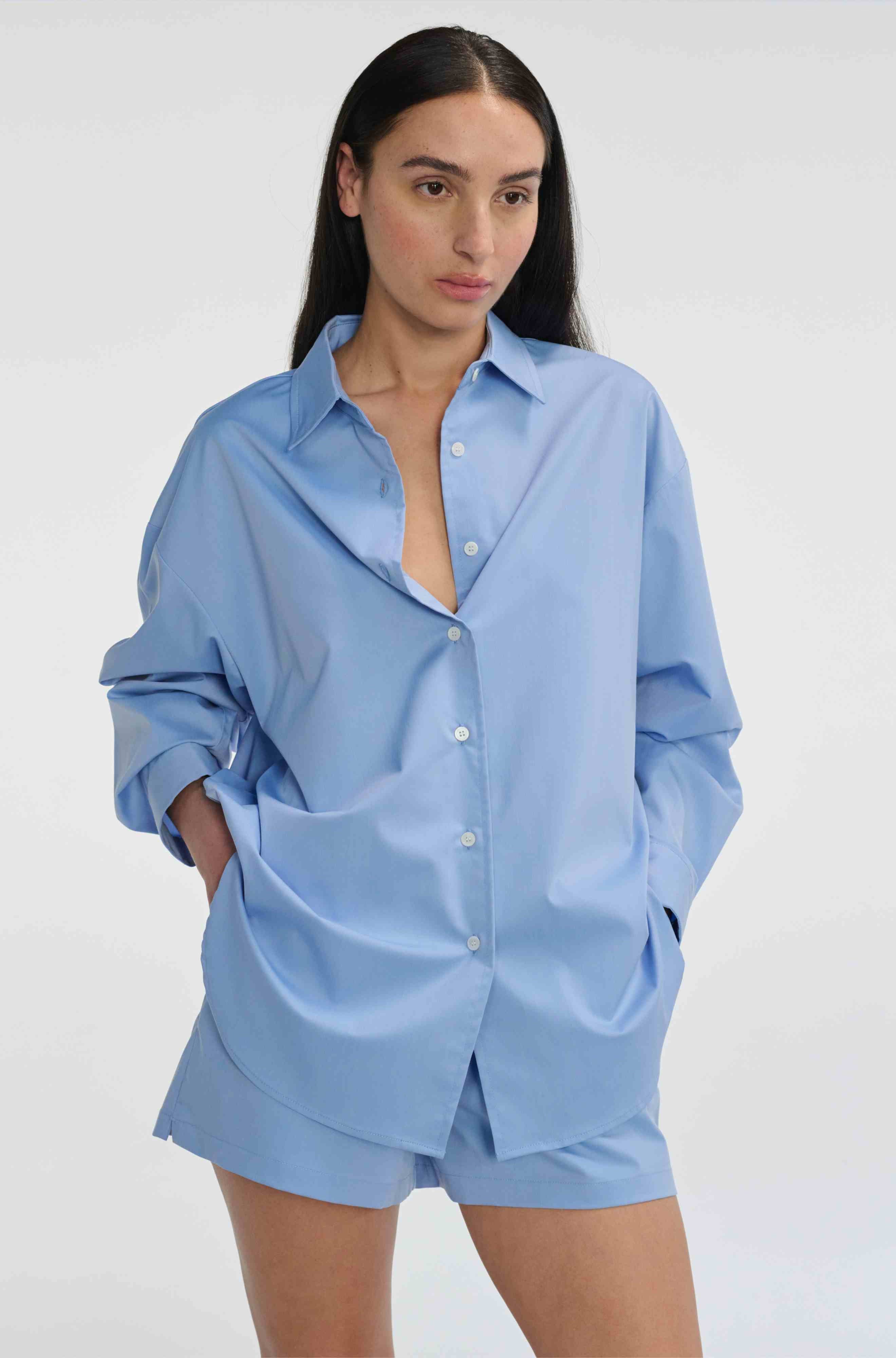 Woman wearing a light blue oversized shirt and shorts on a white background