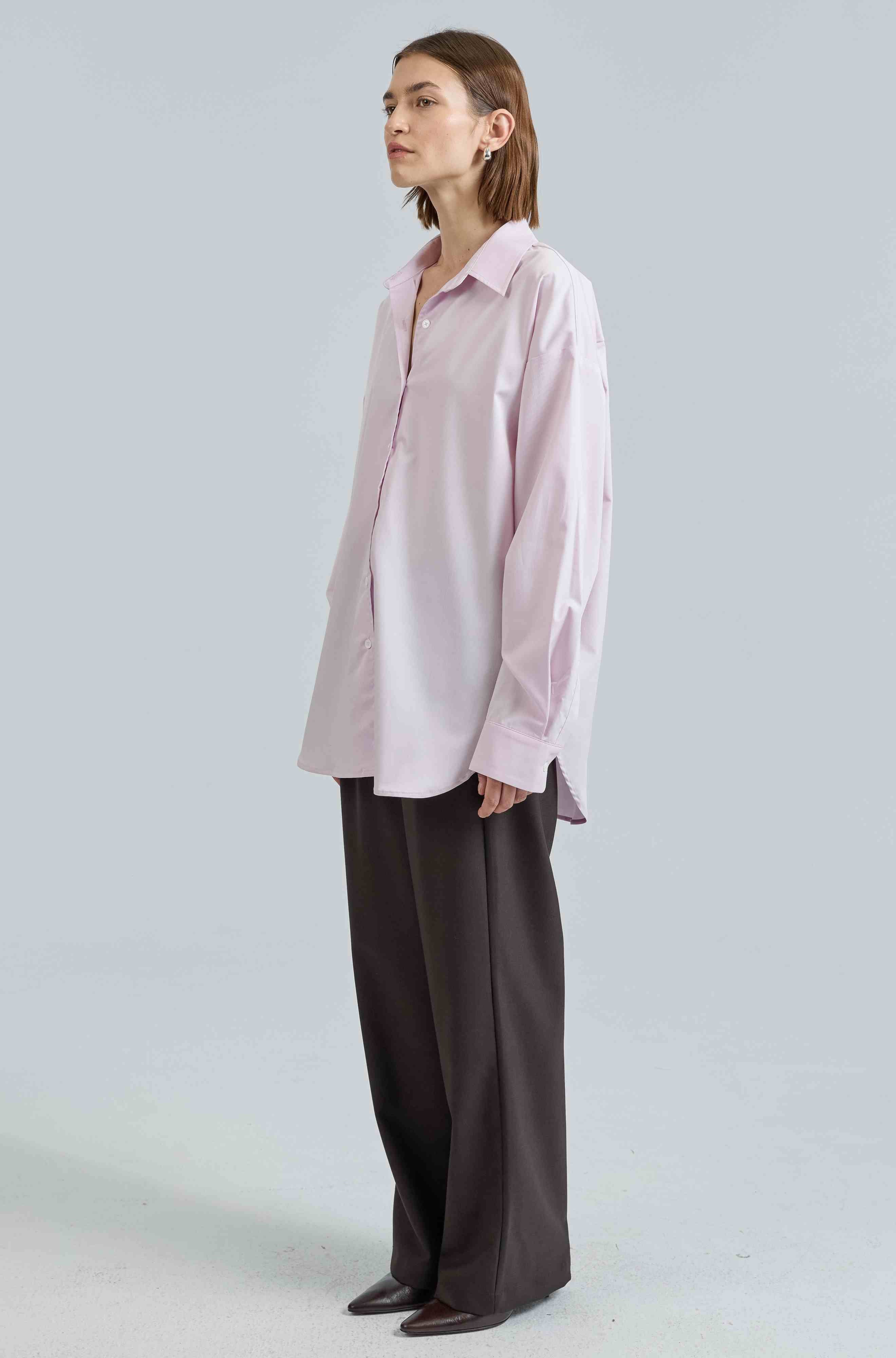 Woman wearing a light pink shirt and dark pants on a white background