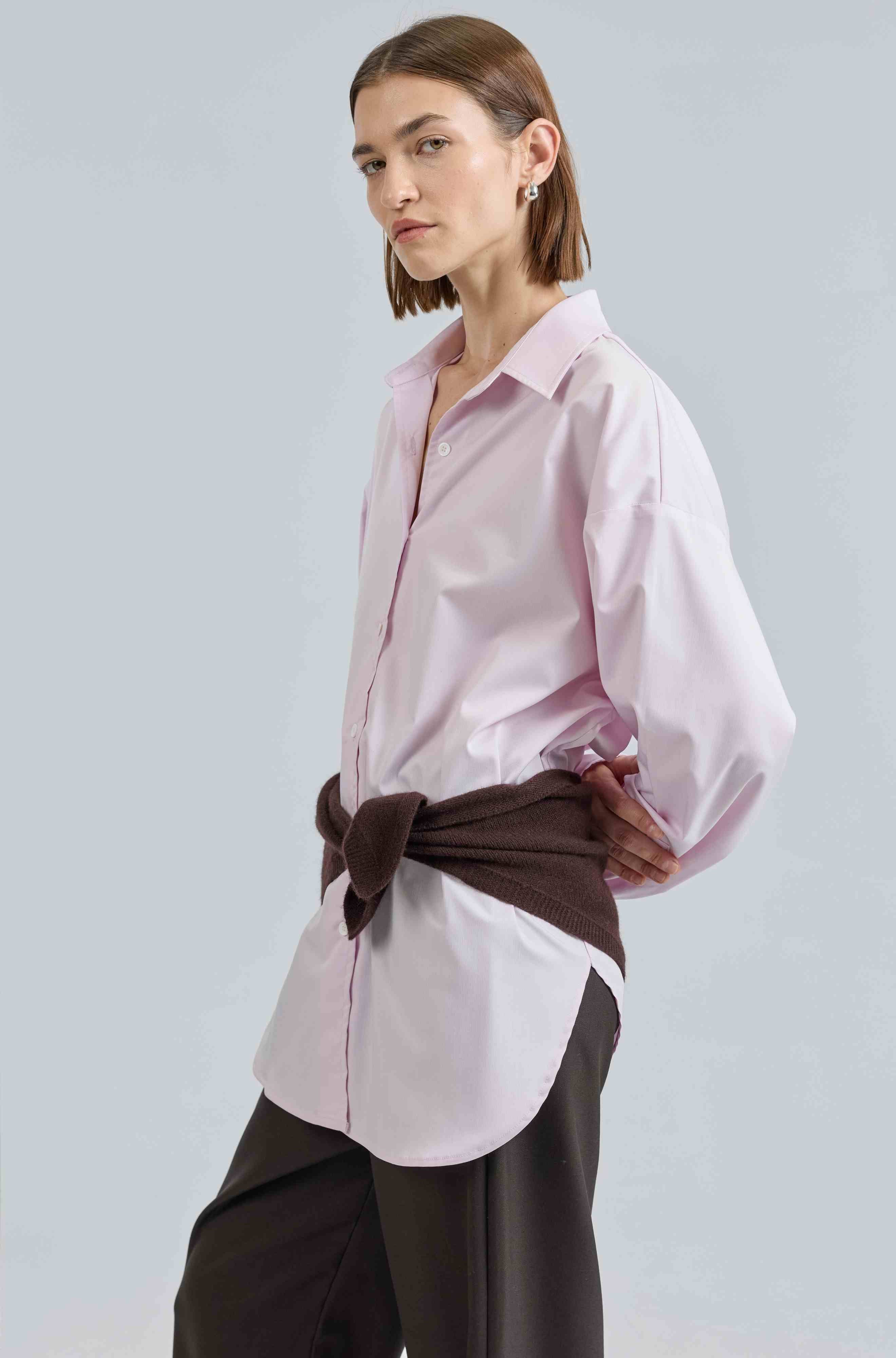 Woman wearing a light pink blouse with a brown belt against a light gray background