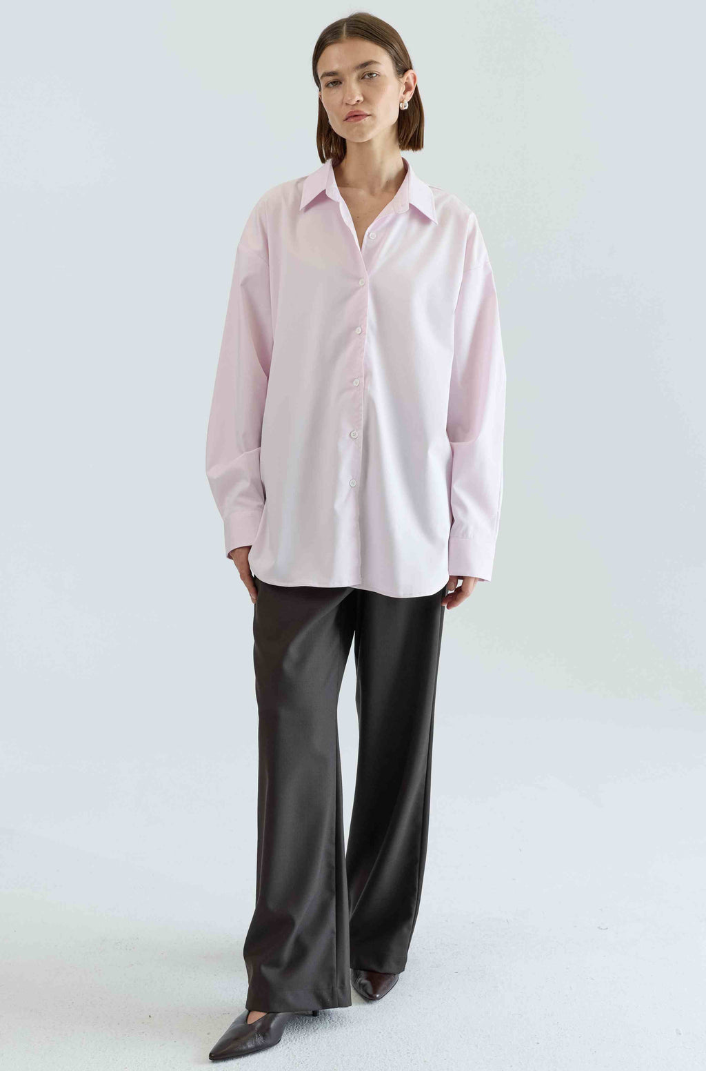 Woman wearing a light pink shirt and black pants on a white background