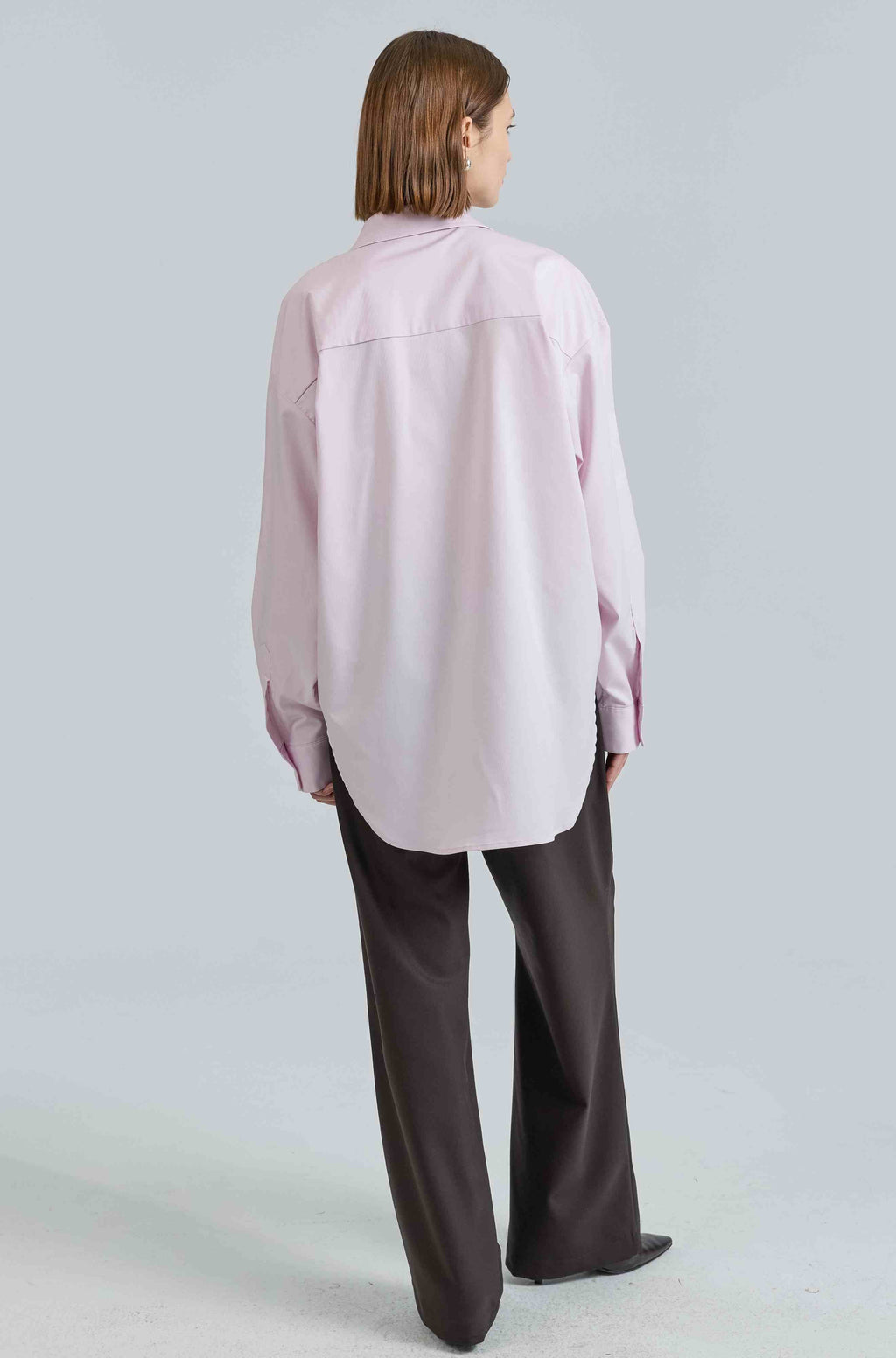 Person wearing a light pink shirt and dark pants on a light gray background