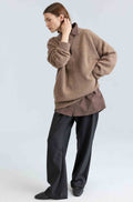 Woman wearing a brown sweater over a dark brown button up shirt and black pants