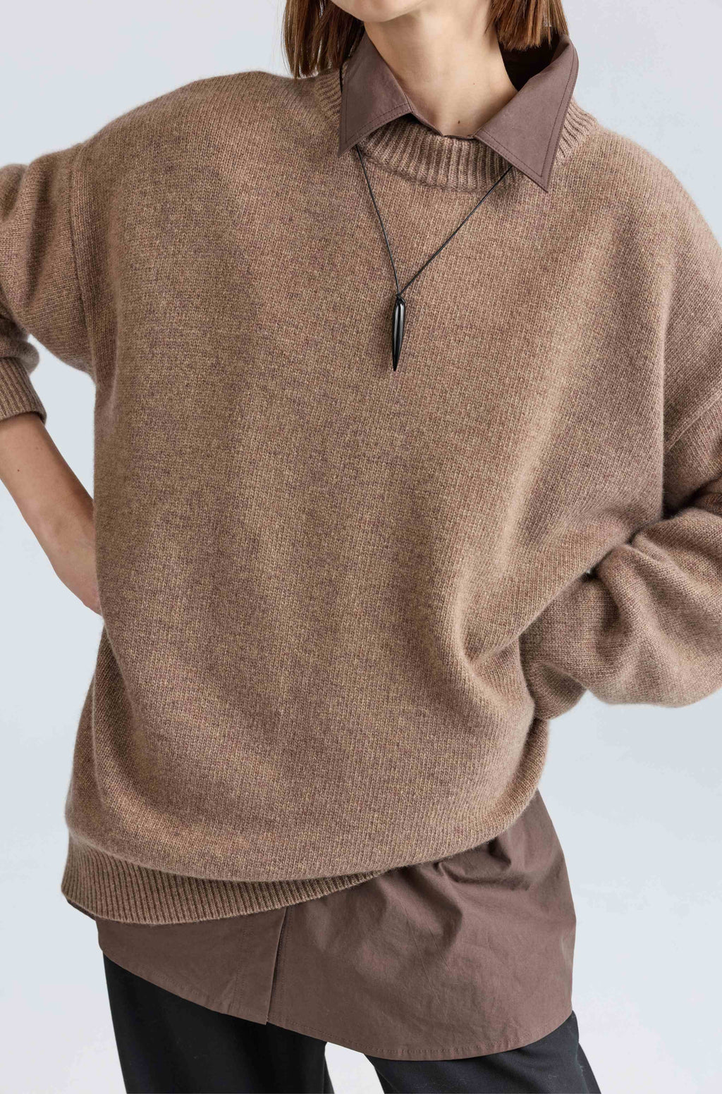 Person wearing a brown sweater and pants with a plain background